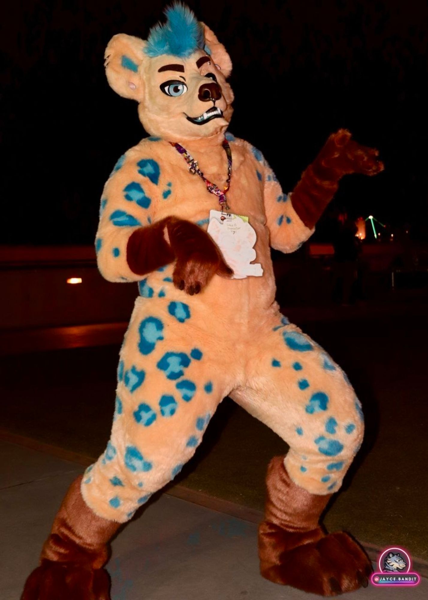 A light brown hyena fursuit with blue spots posing at night