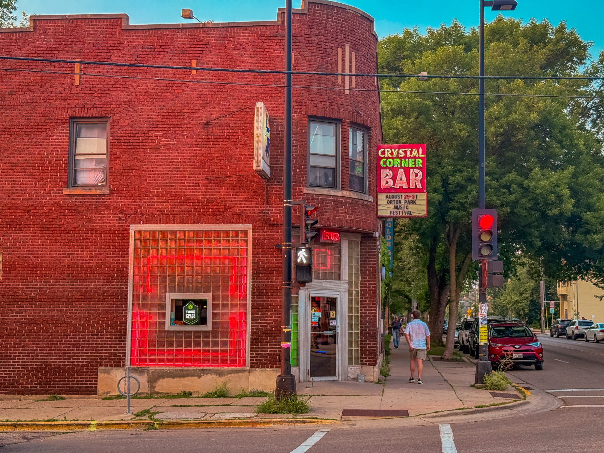 Image of a red brick building with neon lights and a sign at the door designating “Crystal Corner Bar”.  There is a person walking away from the frame on the sidewalk.