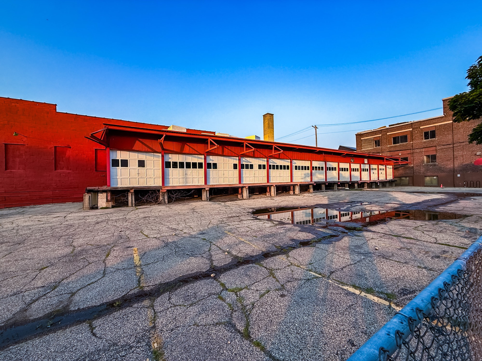 Image of a receiving dock with many white doors across a parking lot.  A chain link fence enters the frame in the lower right.
