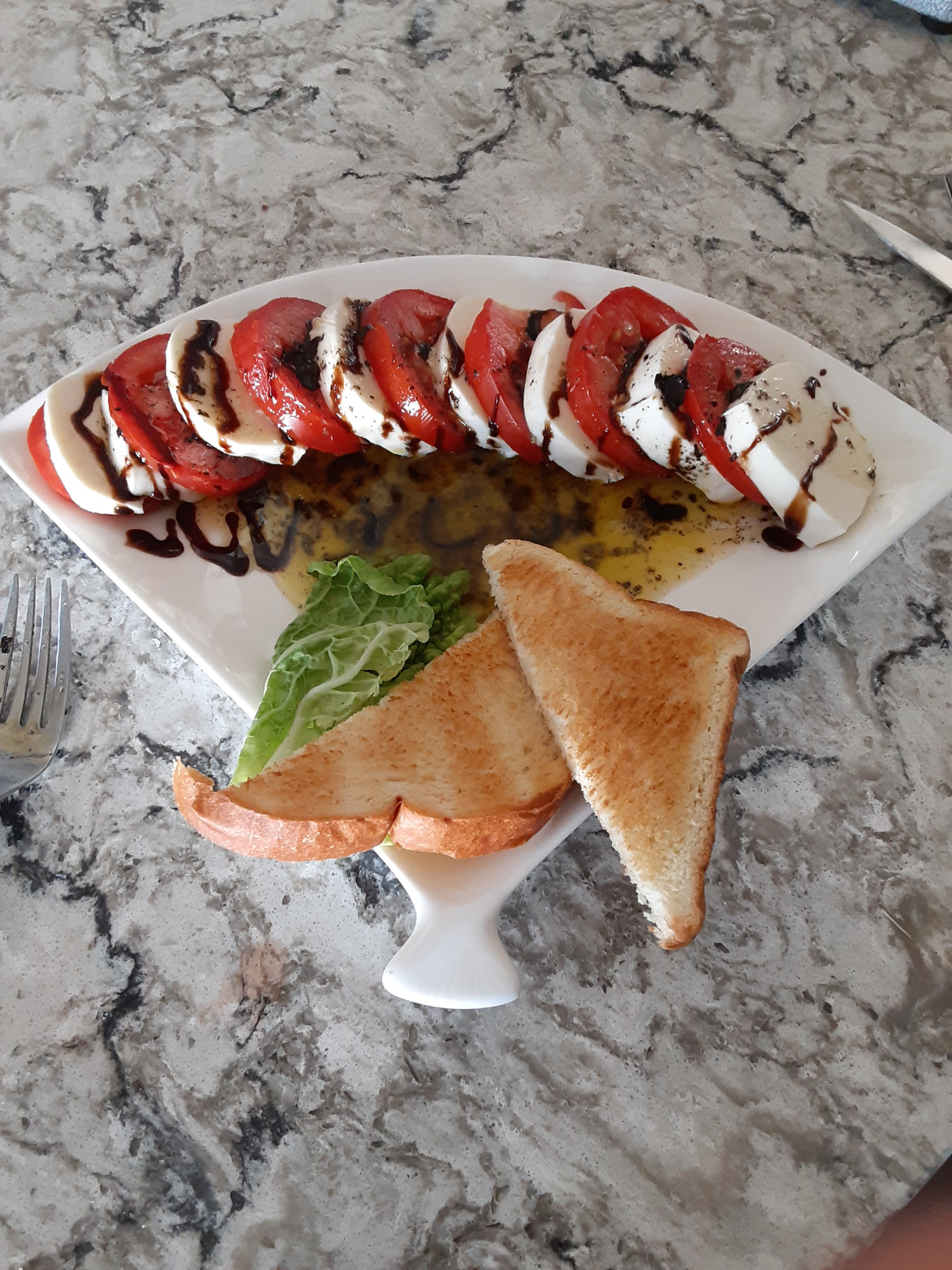 caprese salad drizzled in a basil olive oil and balsamic glaze paired with a piece of lettuce for decoration and two slices of white toast