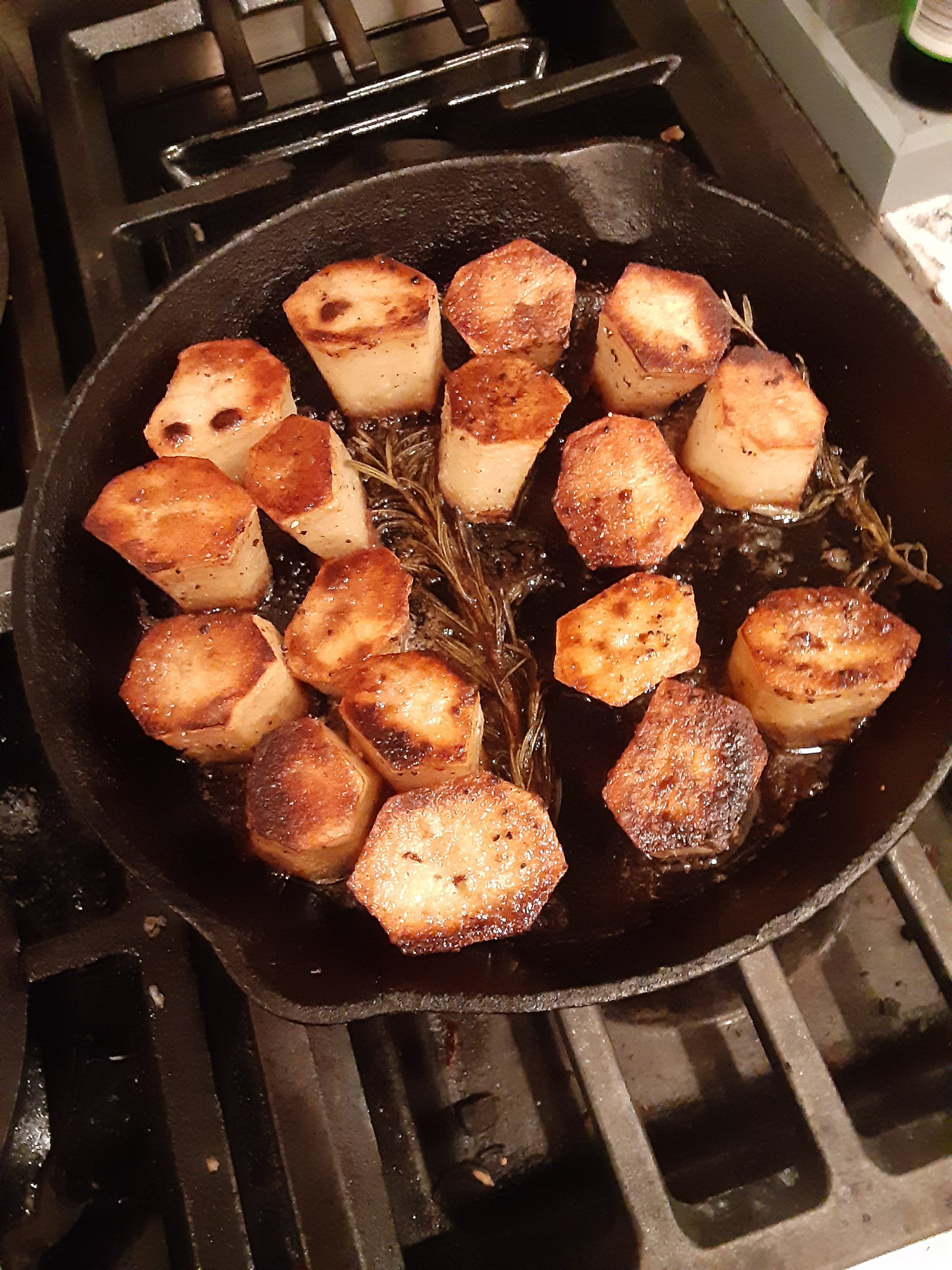 fondant potatoes in a cast iron pan with fresh rosemary and thyme