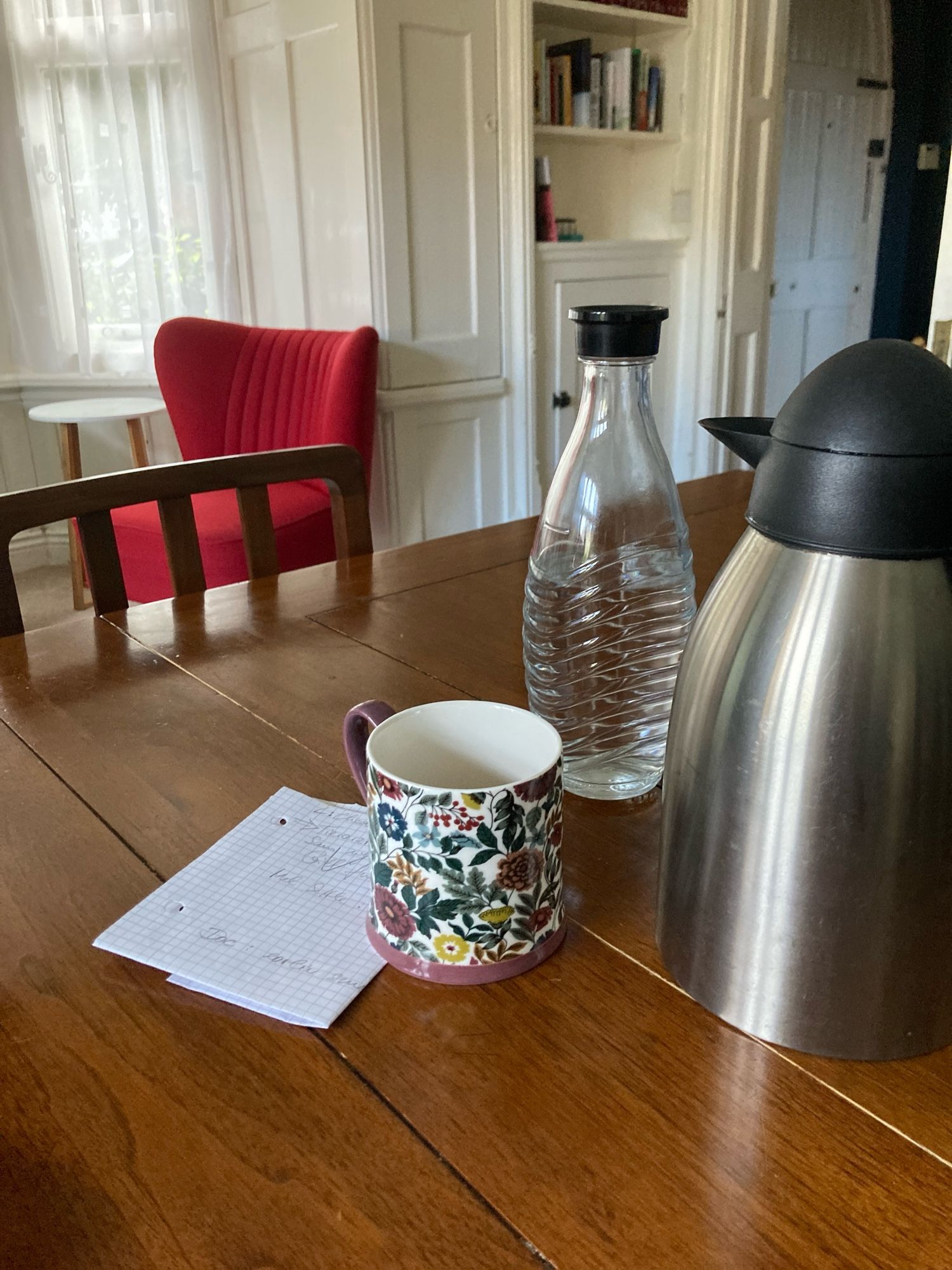 A large kettle shaped thermos flask next to a mug with floral design on a wooden table