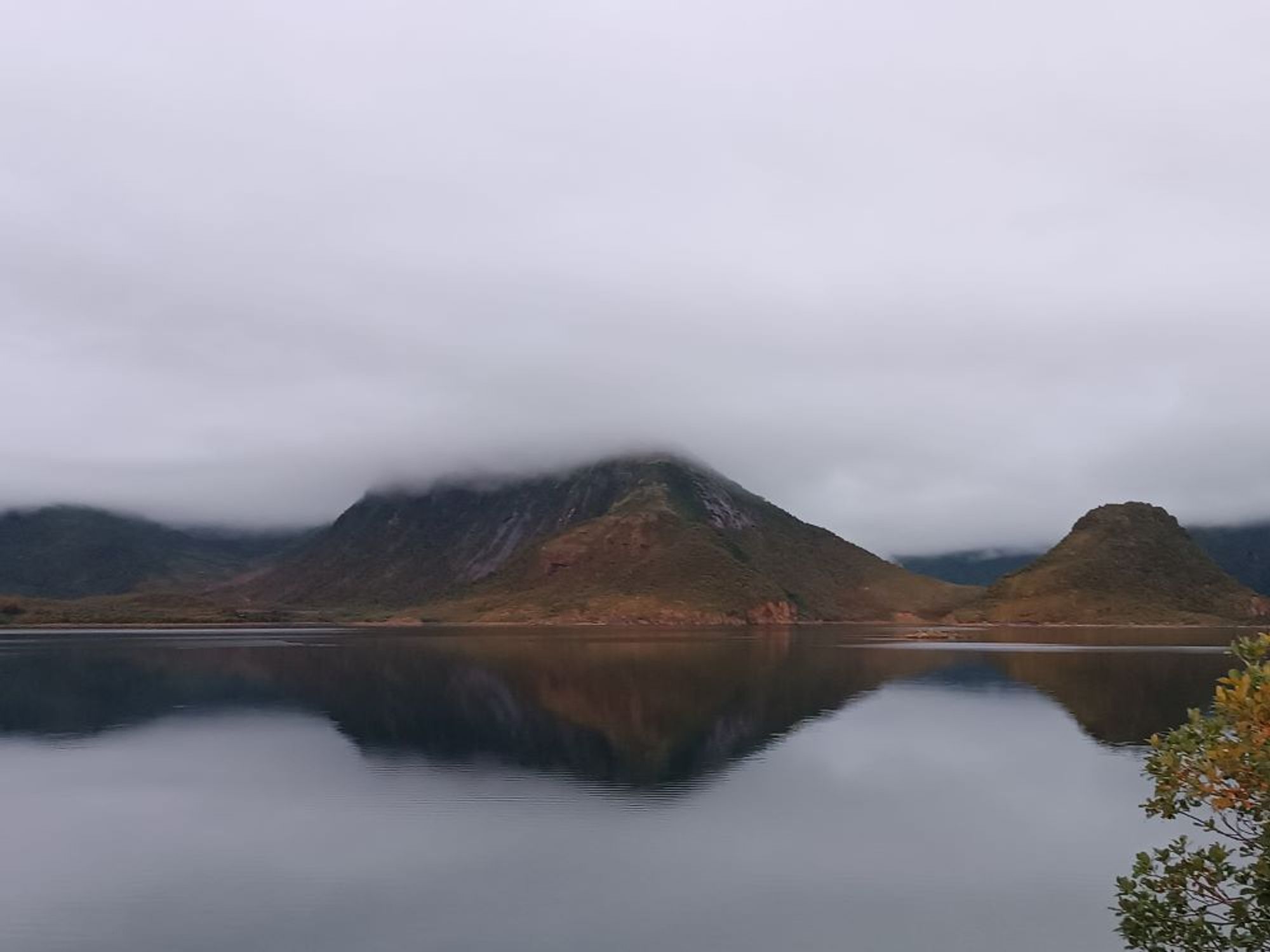 eine norwegische Hügellandschaft im See gespiegelt mit Wolken an Bergspitzen, braungraue Berge