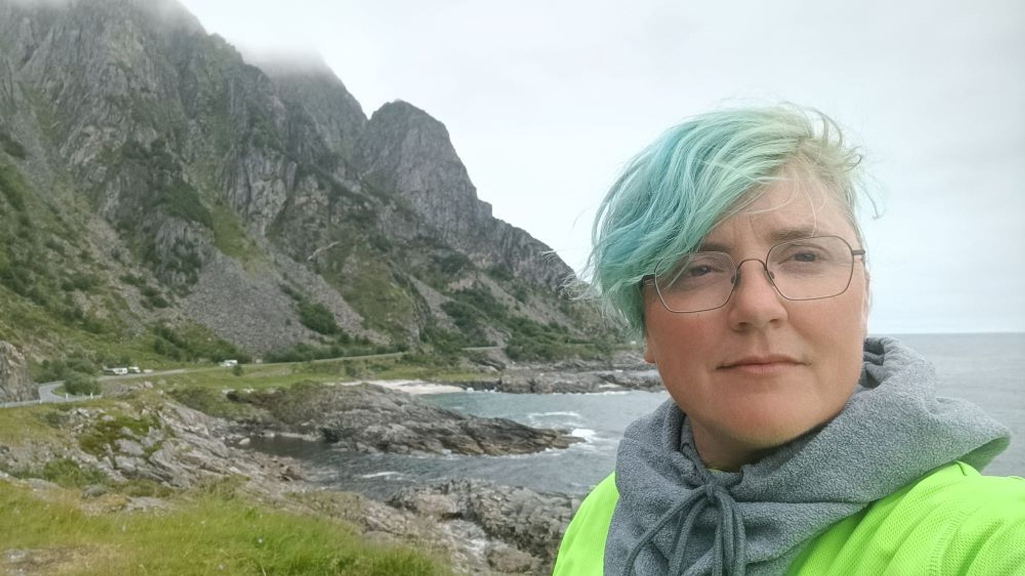 ich schaue ernst in die Kamera und stehe vor gewaltigen Felsen am meer in Norwegen