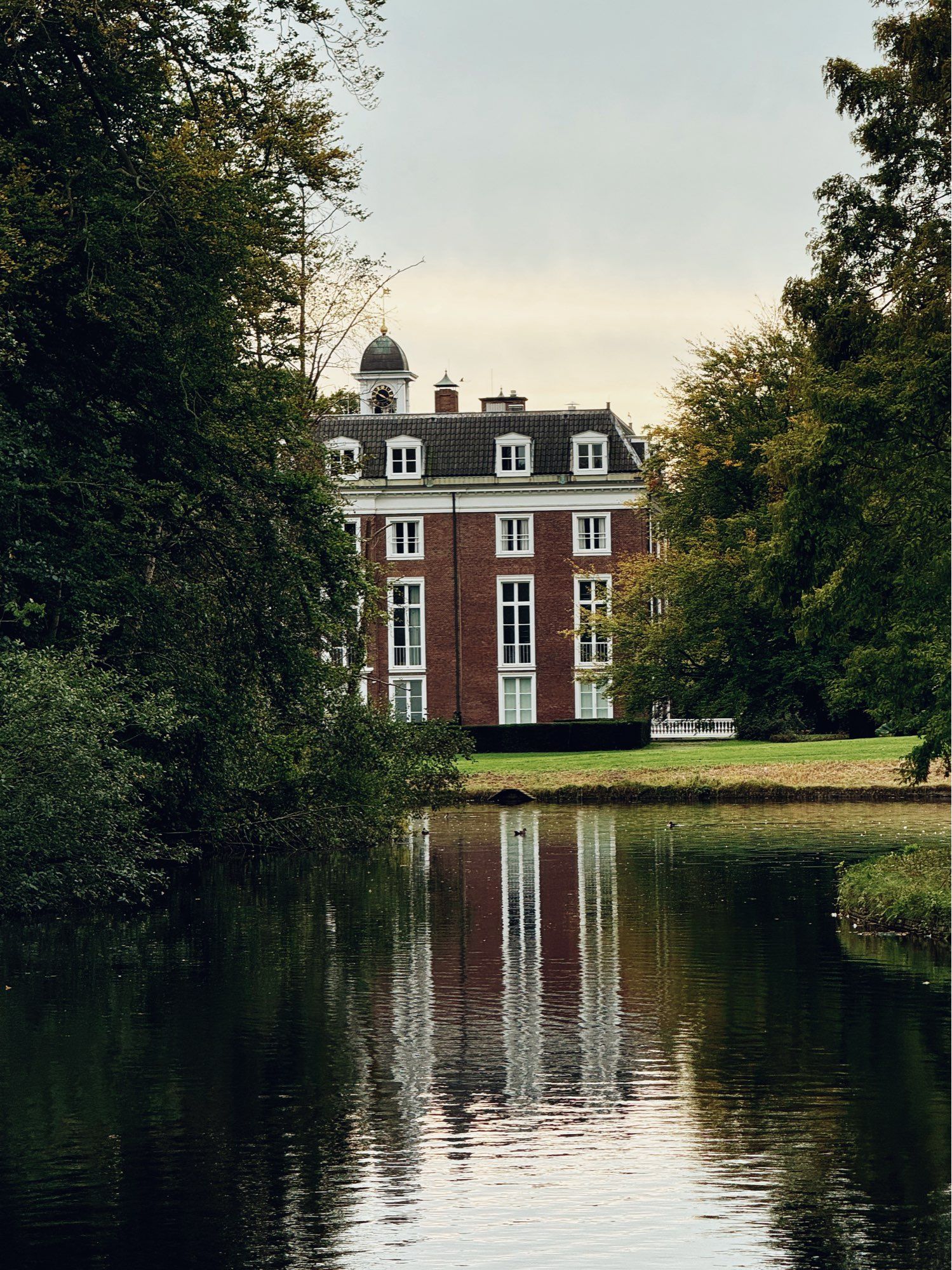 Clingendael manor house half hidden by trees and reflected in the water.