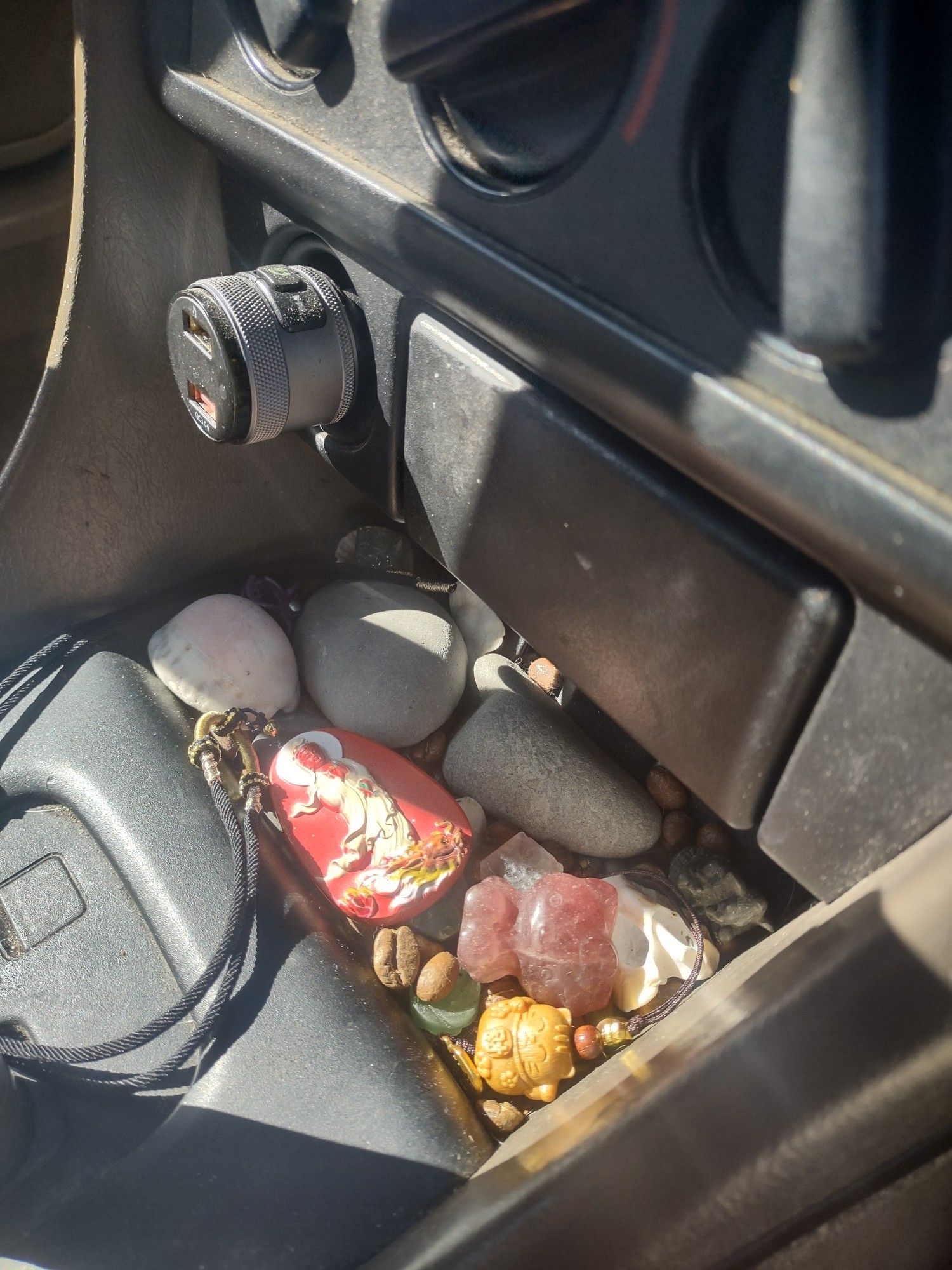 Some rocks, a quanyin medallion, a hello kitty carved from a crystal, a wooden lucky cat, coffee beans and seaglass in Kitty's car