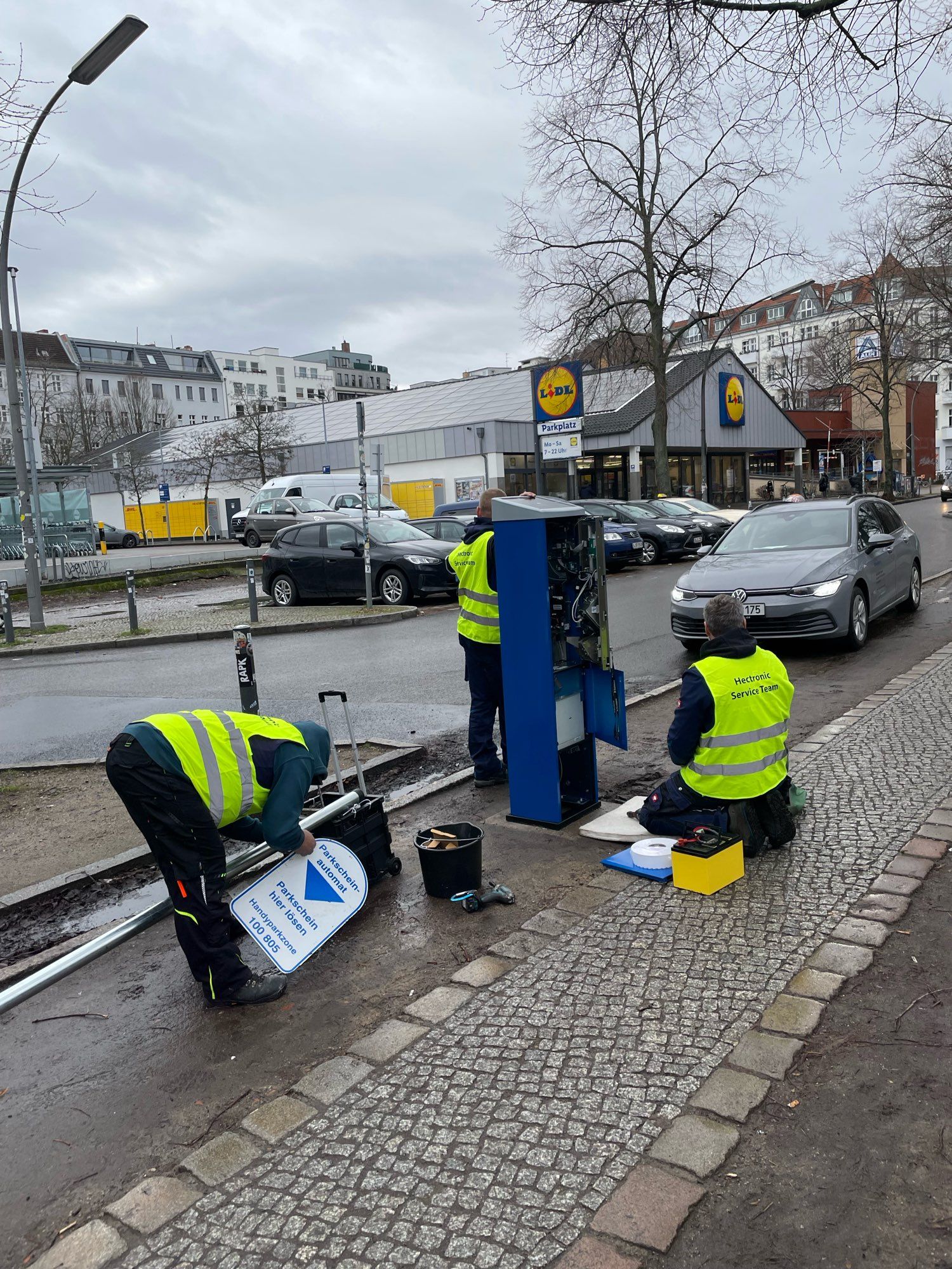 Foto von Bauarbeiten am Maybachufer, Neukölln:  drei Männer installieren einen Parkscheinautomaten.