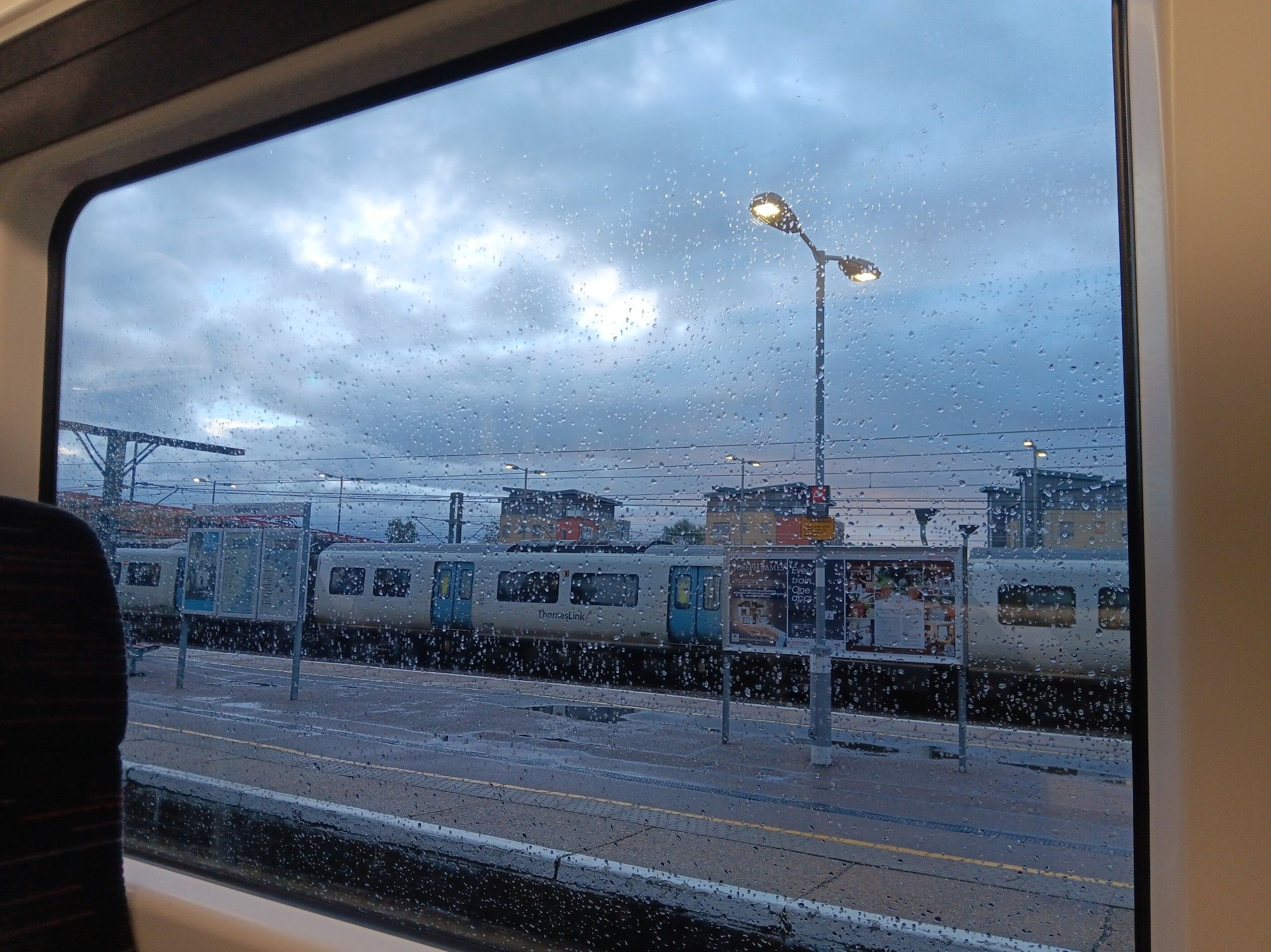 View from a train on platform 6 at Cambridge station, with platforms and another train. It's cloudy and wet.