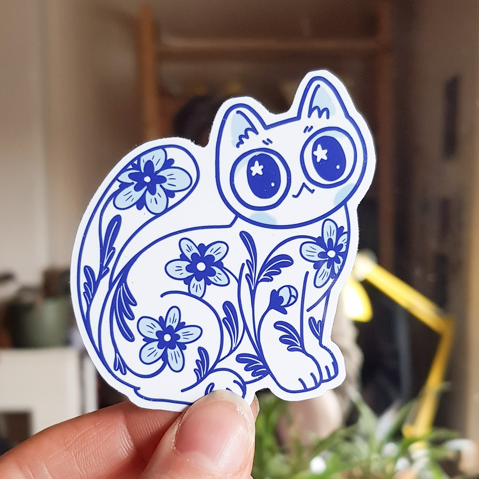 Photo of a sticker of a porcelain style white and blue cat decorated with flowers - cat is sitting and looking ahead