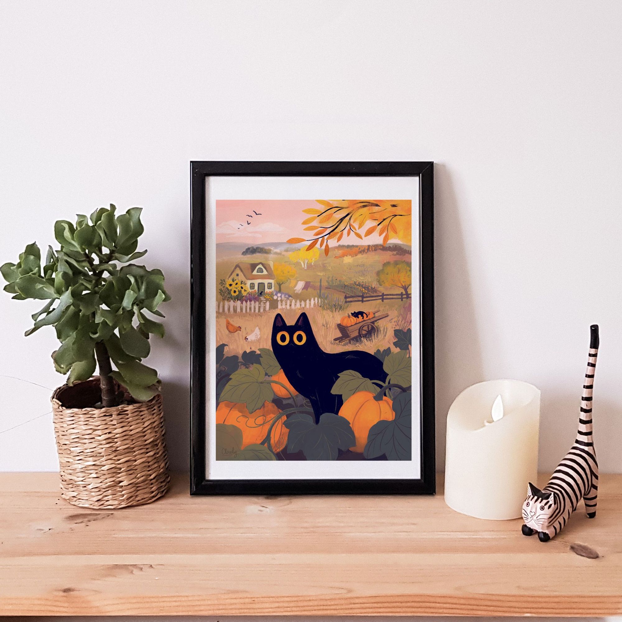 a photo of a framed print from the previous post sitting on a shelf with a plant, a candle and a cat figurine