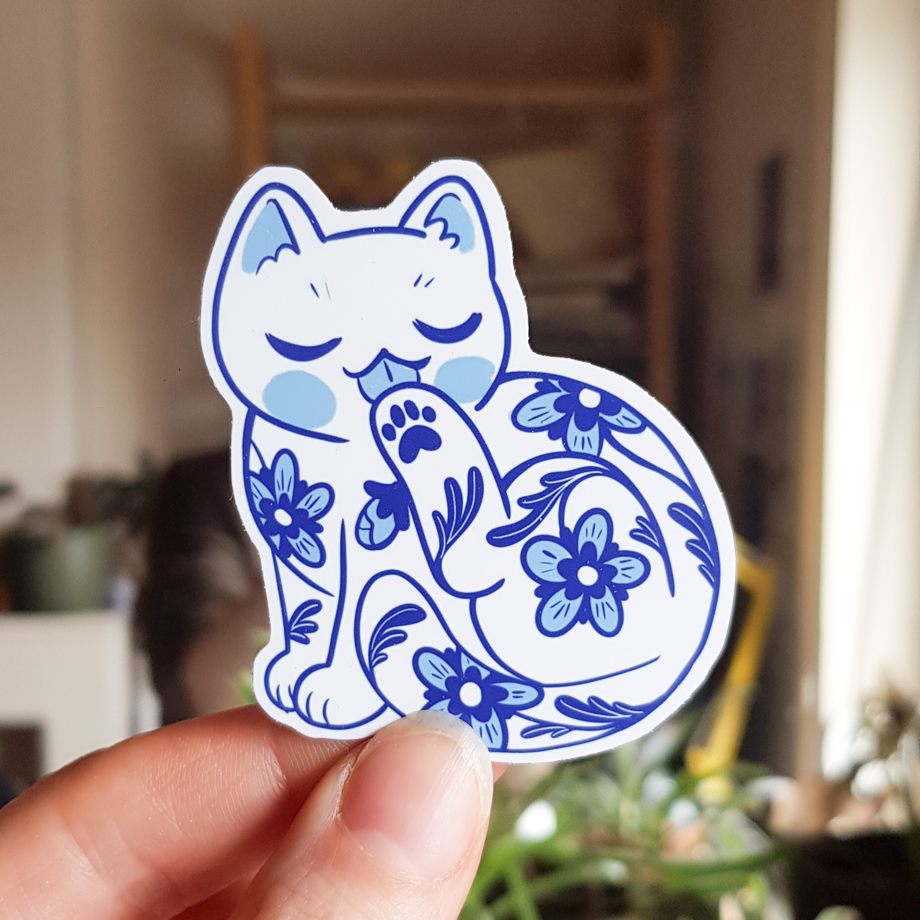 Photo of a sticker of a porcelain style white and blue cat decorated with flowers - cat is grooming it's paw