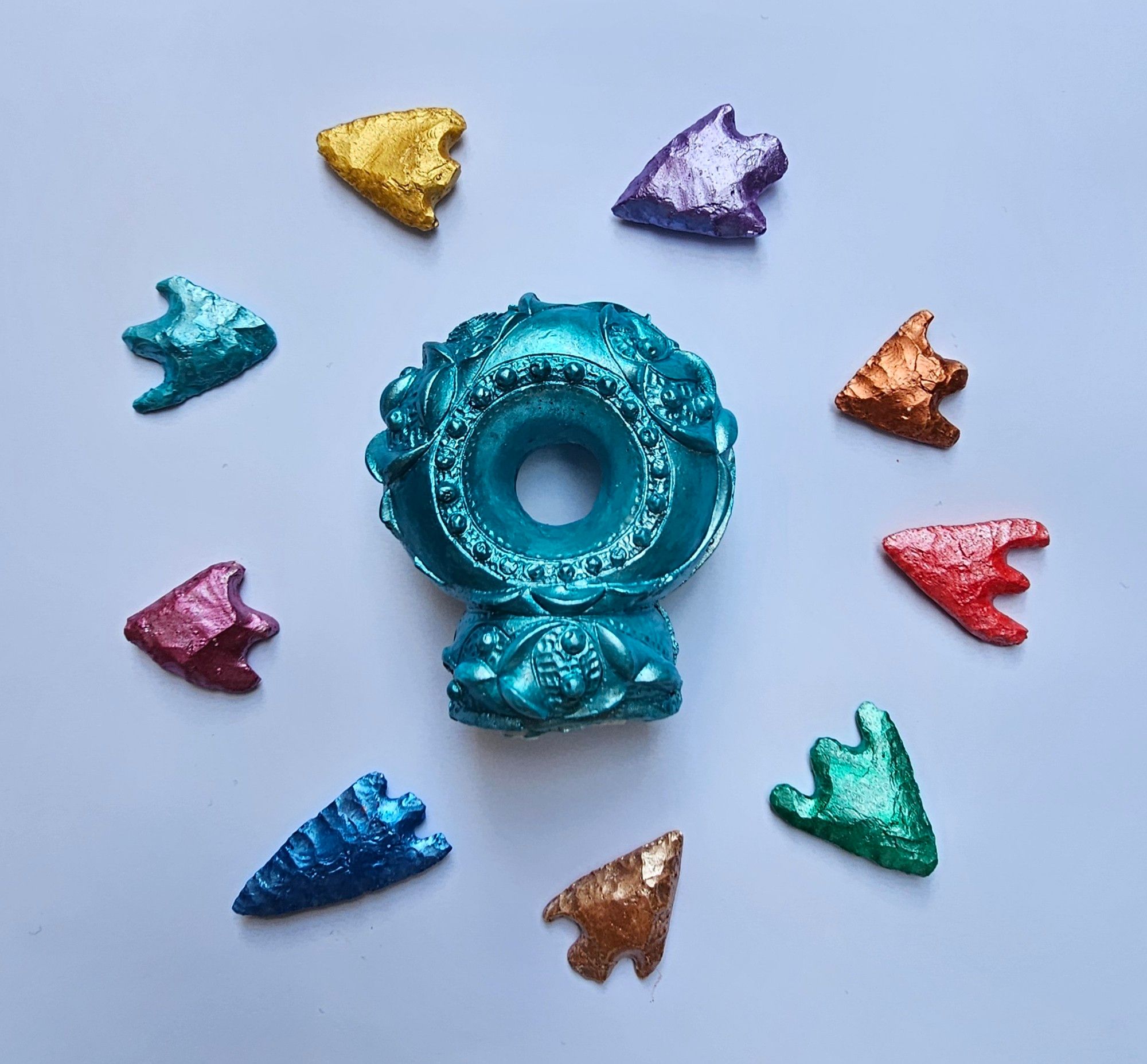 A circle of rainbow metallic arrowheads with a metallic aquamarine Netherurd torc terminal in the centre