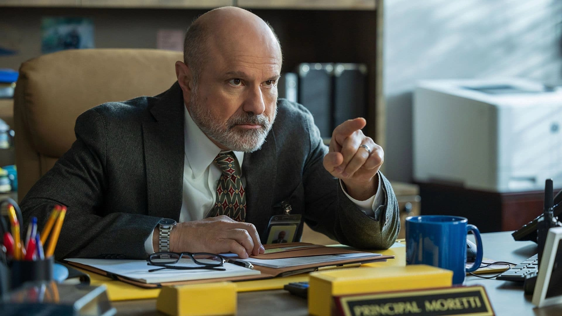 Enrico Colantoni in “English Teacher” sitting at his principal’s desk and pointing at someone seriously 