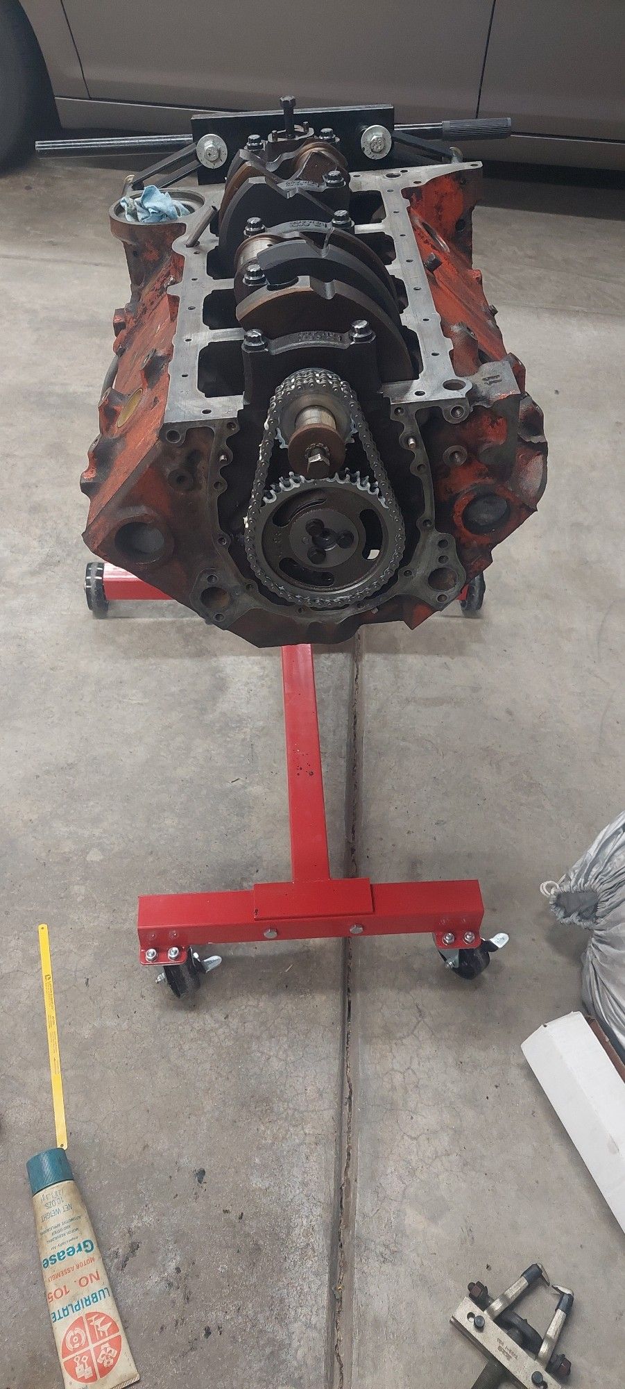 A heavily patina'ed first gen small block chevy V8 upside down on a stand. It has a bolted in crank shaft attached to the timing set and camshaft. Nothing else is attached to the engine.