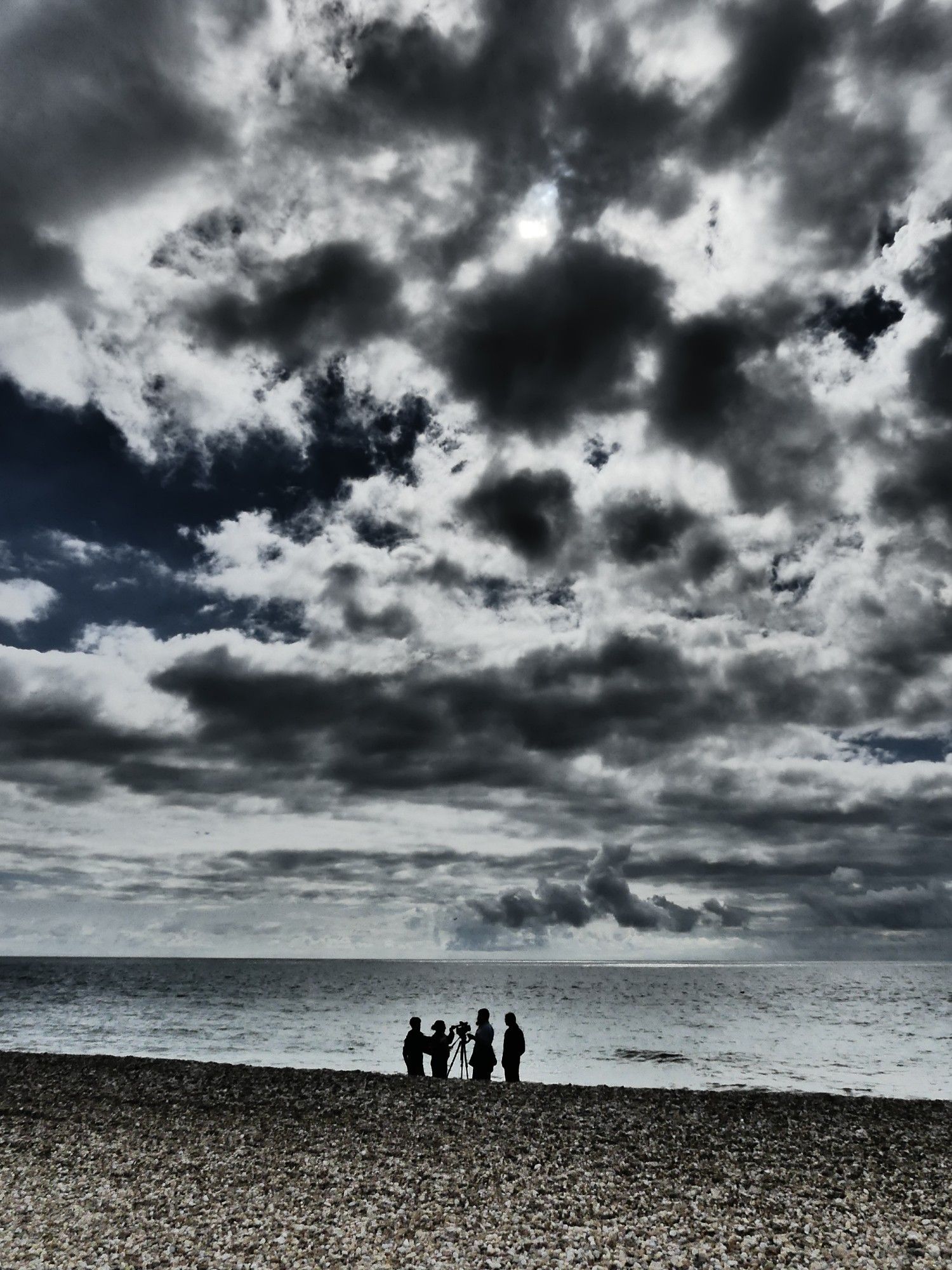 Silhouetted figures with movie camera on a shingle beach with dramatic sky