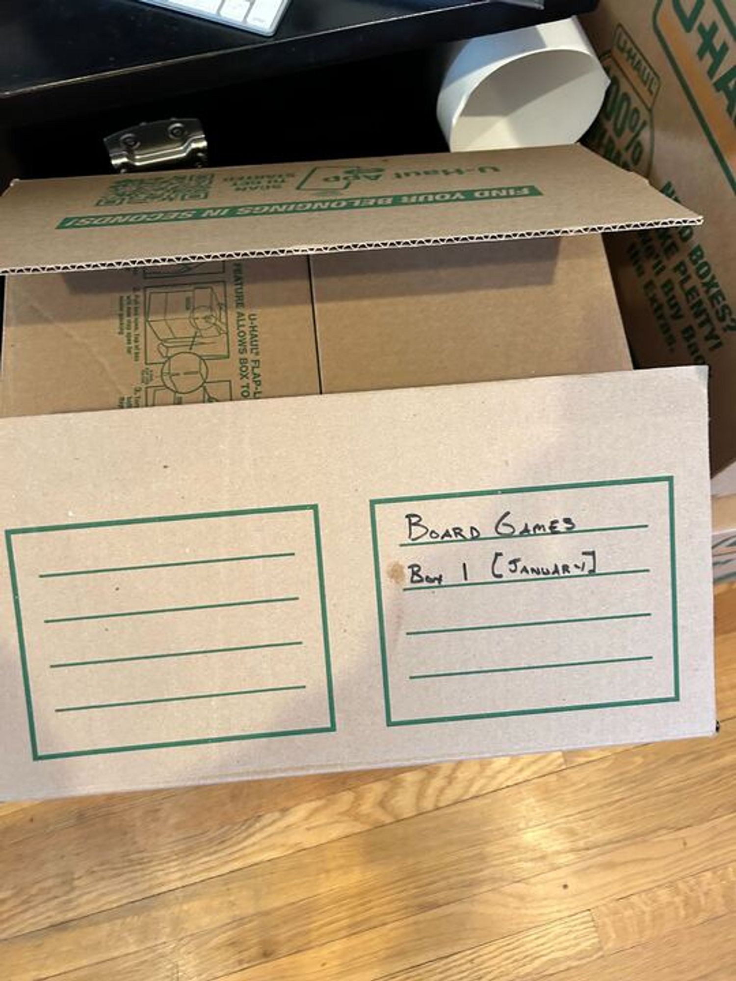 A brown UHaul packing box with handwritten "Board games, Box 1 [January]" written on the top.