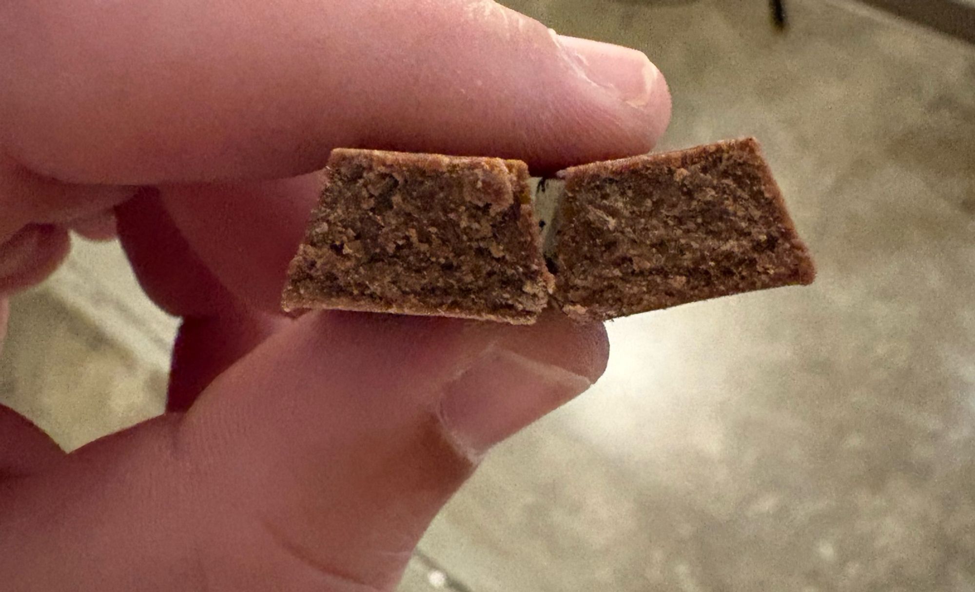 Photo of two fingers holding a small KitKat bar broken in half, showing that it was solid chocolate with no wafers inside