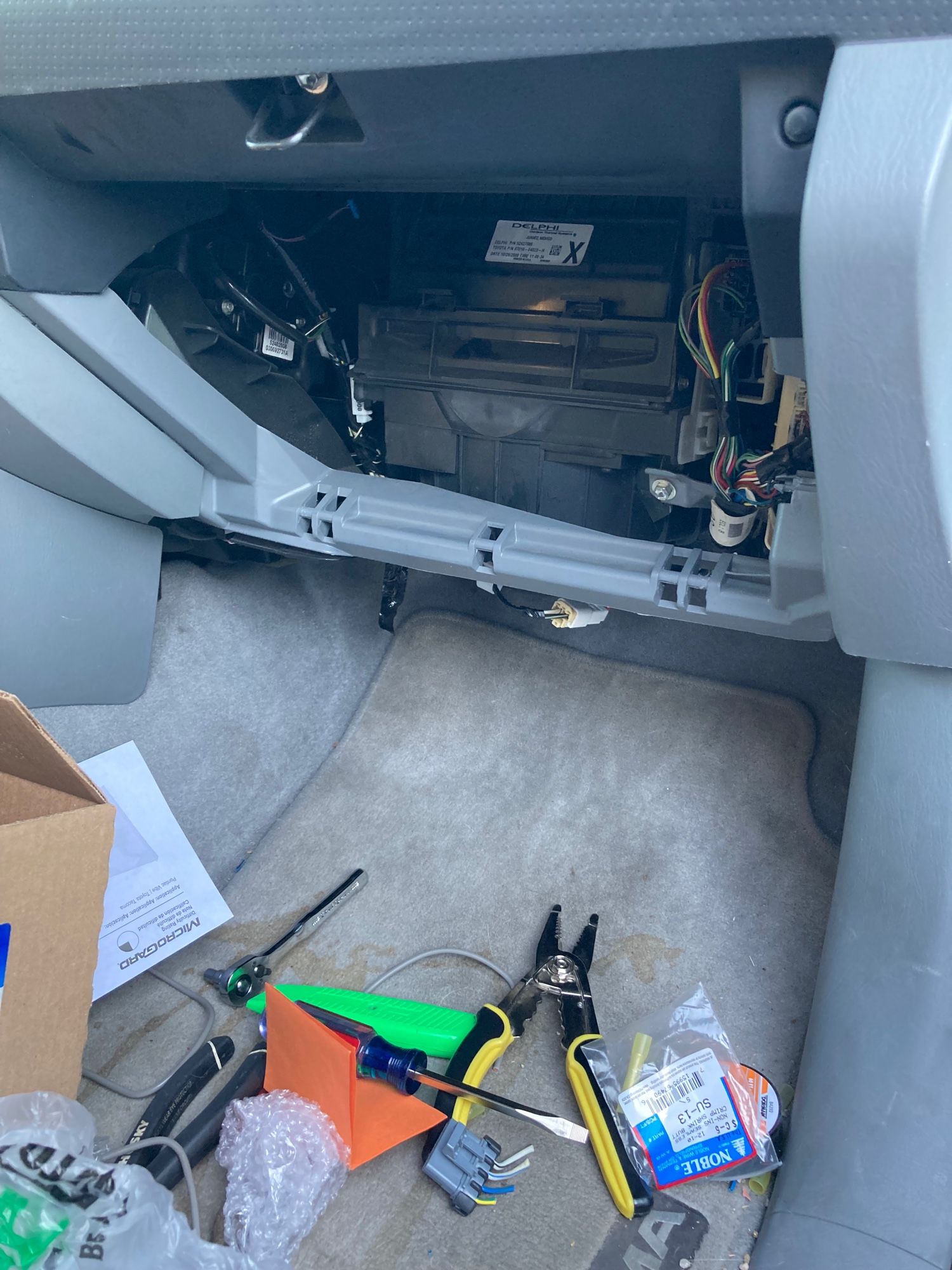 The passenger-side footwell of a Toyota Tacoma strewn with tools (screwdriver, wire cutter/strippers, socket wrench, etc) and debris (scraps of wire, a cut-off electrical connector, and discarded packaging). 

The glovebox has been removed from the dash to reveal a couple of small bundles of electrical wires and the A/C blower (a lumpy black plastic thing taking up most of the space in this behind-the-glovebox cavity)