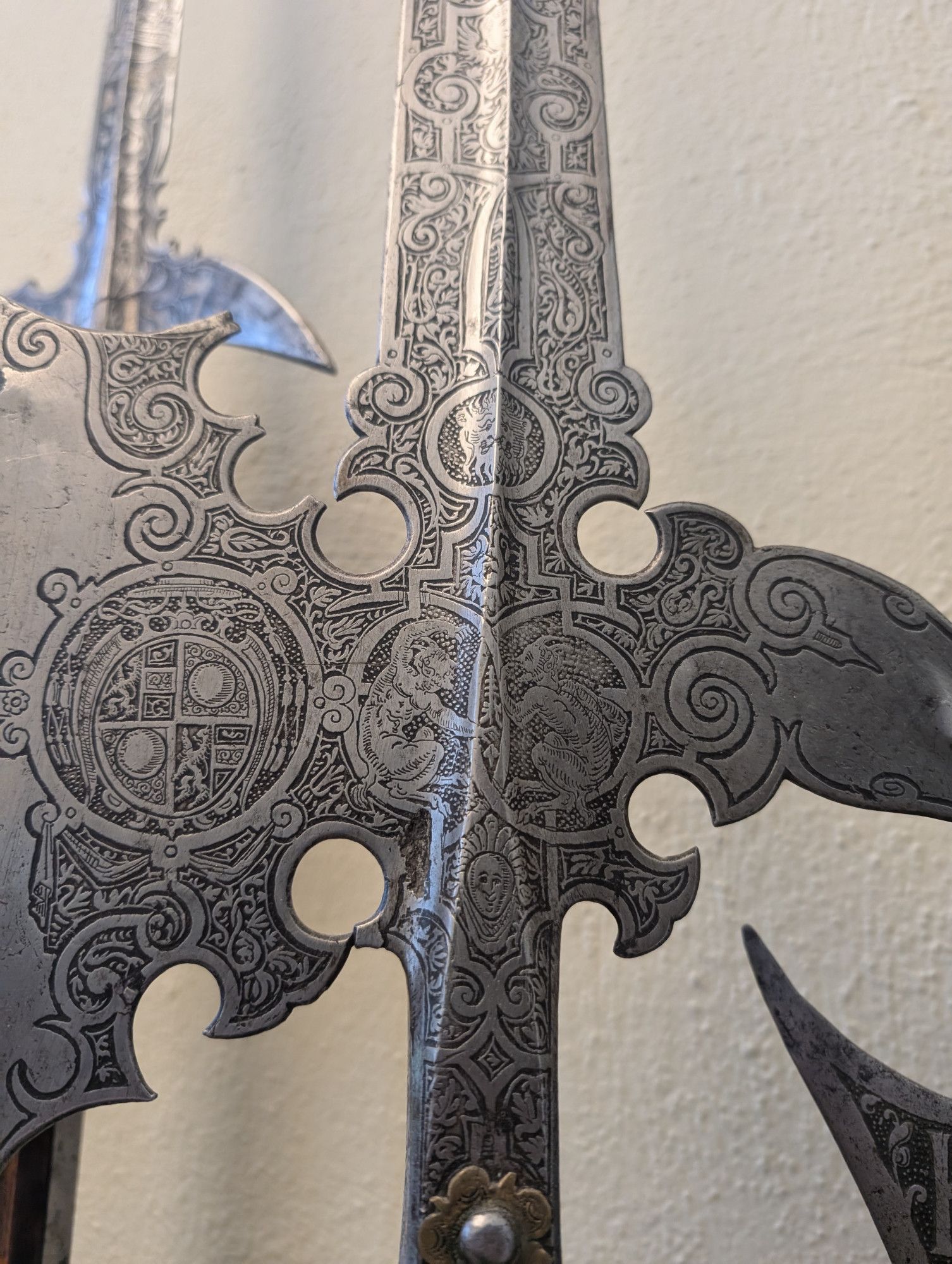 An extremely ornate ceremonial halberd head showing etched and blackened designs with various plants, mythical creatures, and heraldic designs.