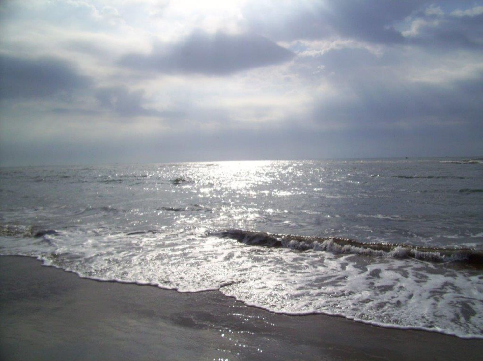 Grey overcast sky with rays of sunlight breaking through, bathing the grey sea below with the colours of molten pewter and silver