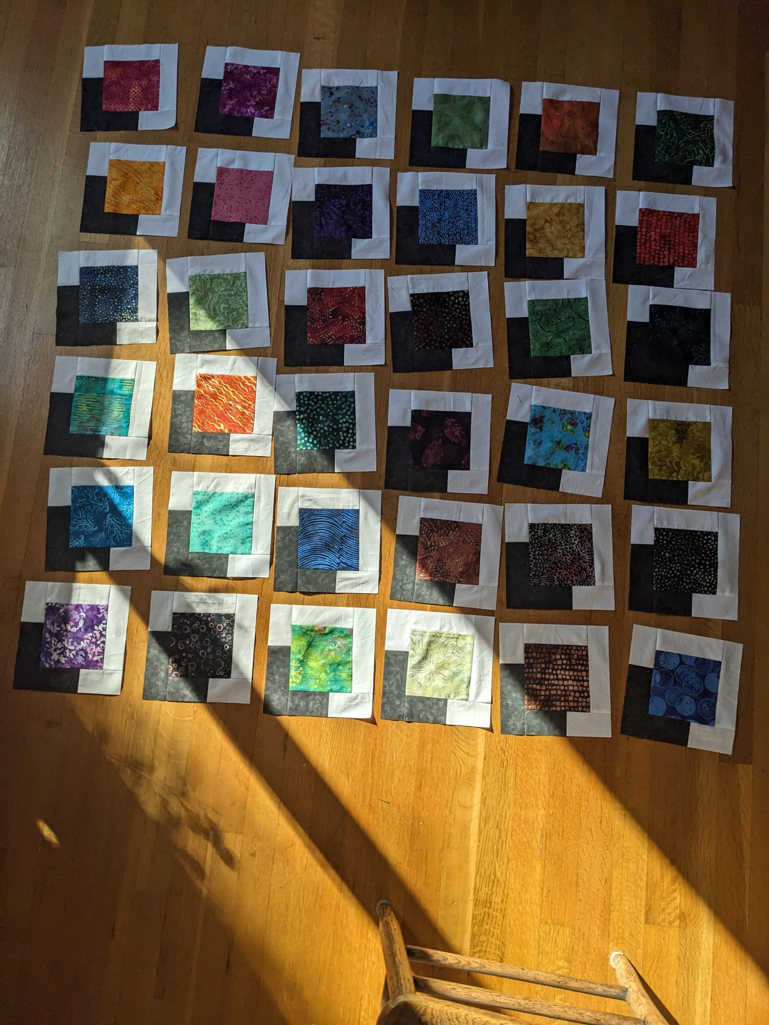 36 quilt blocks, each with a vividly colored square in the center, surrounded by white and a black corner that looks like the colored block is casting a shadow