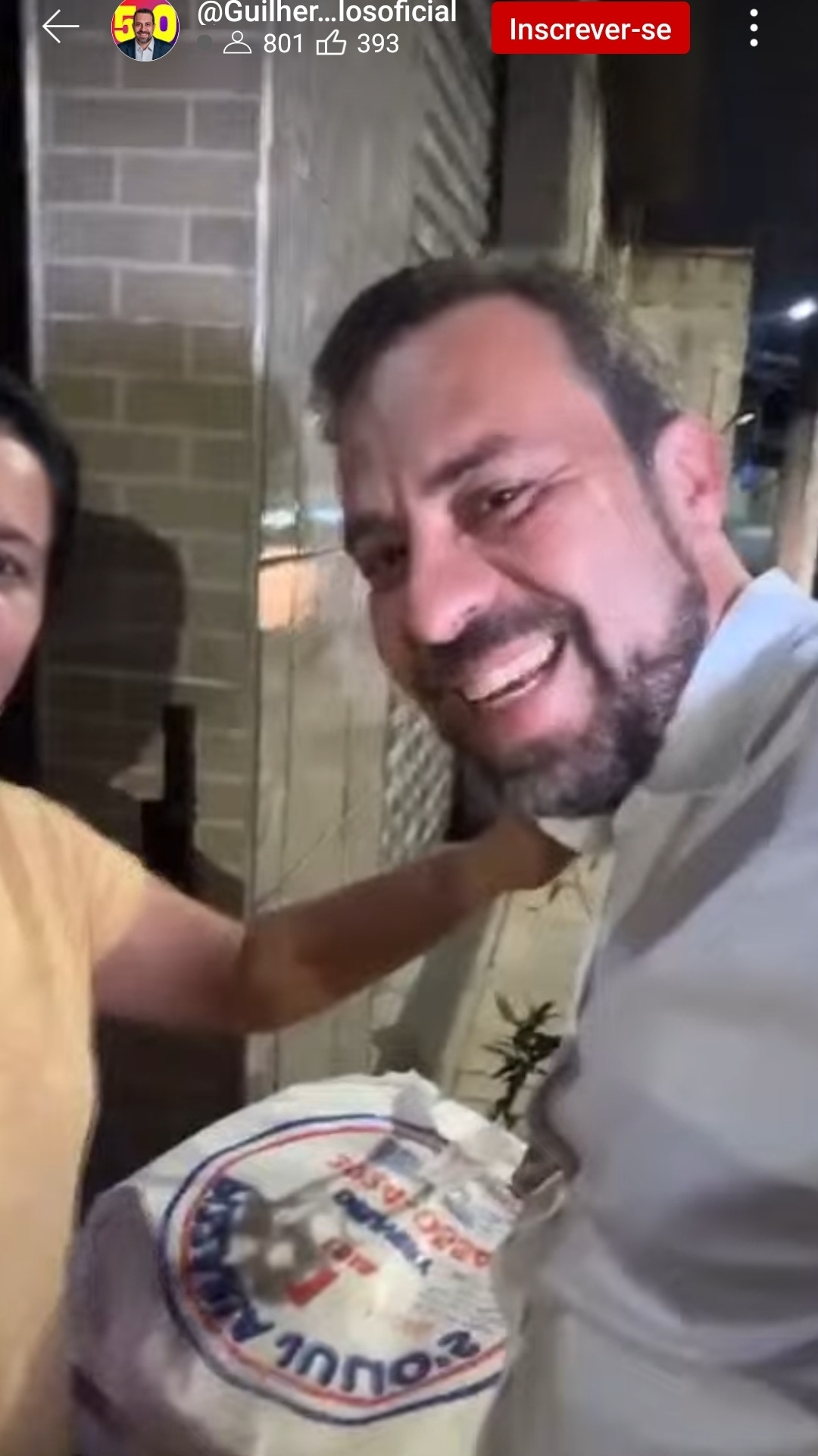 Imagem do Guilherme Boulos em live chegando na casa da mulher sorrindo e com 2 pizza na mão.