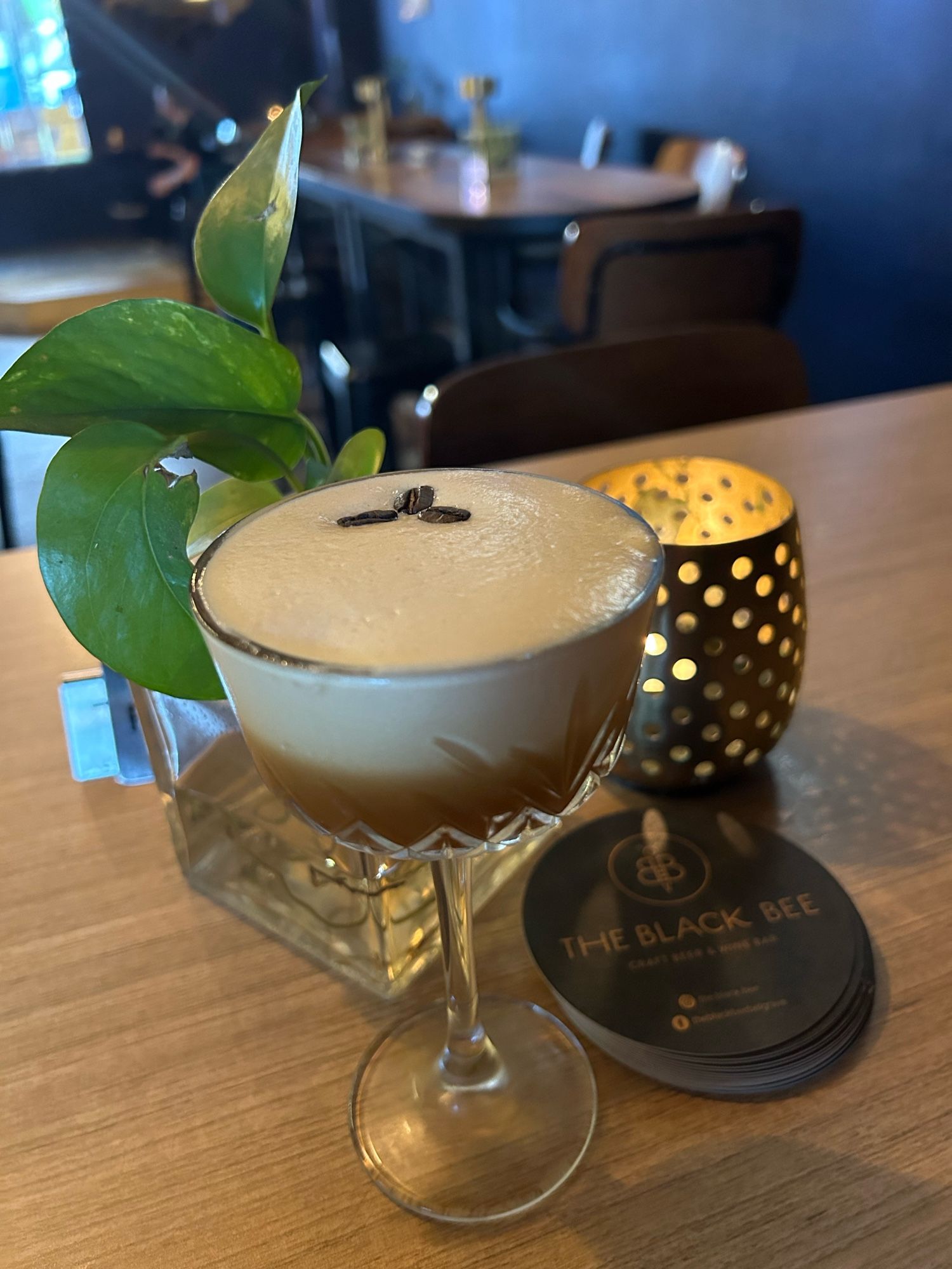 An espresso martini, a tea light candle, and a tiny plant in a jar on a table