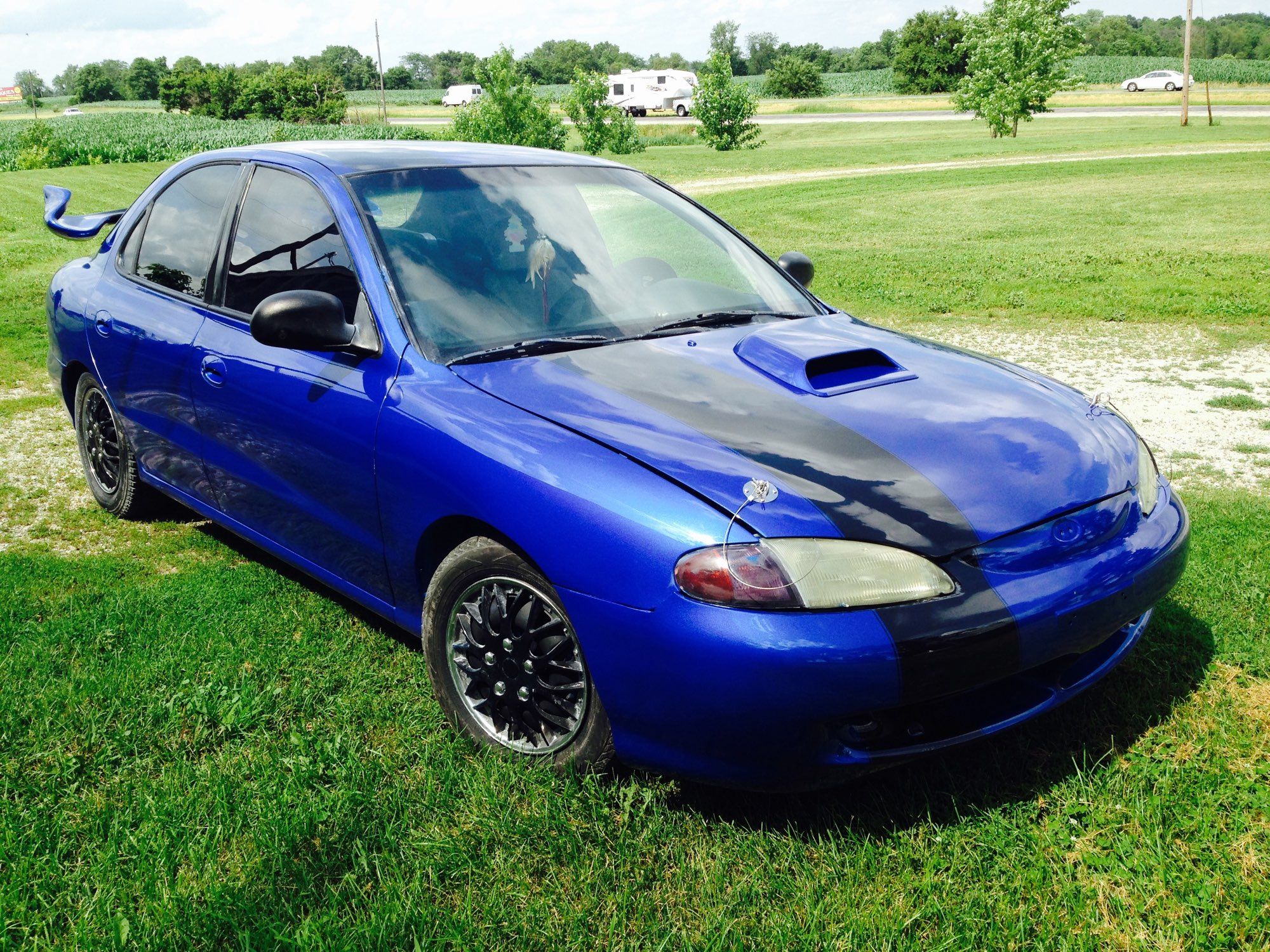 A photo of my car, a blue ‘98 Hyundai Elantra with a black offset stripe down the body.