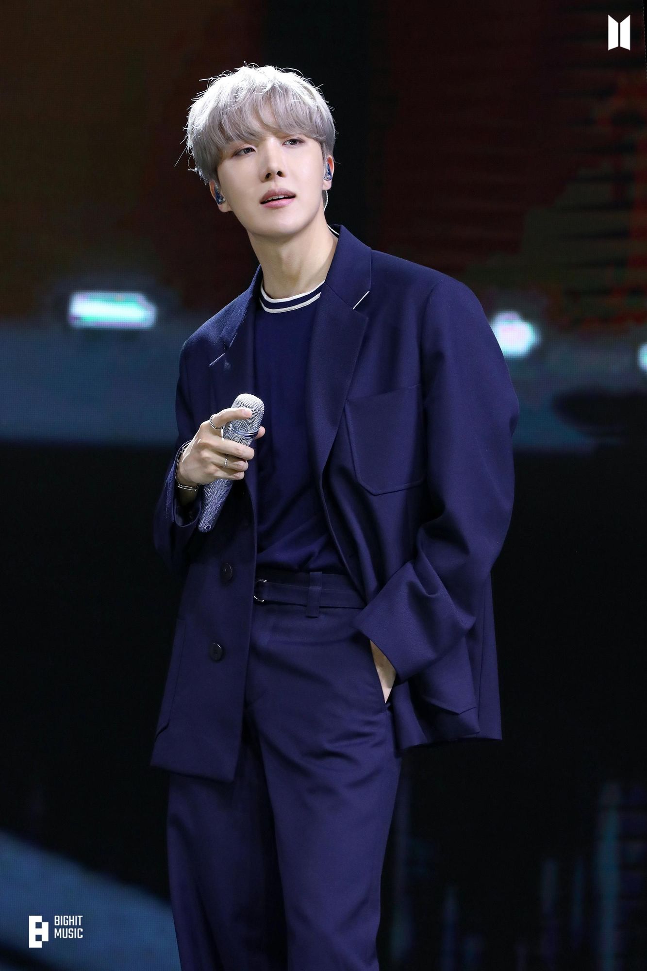 Hobi on stage with a microphone. He's wearing a blue suit.