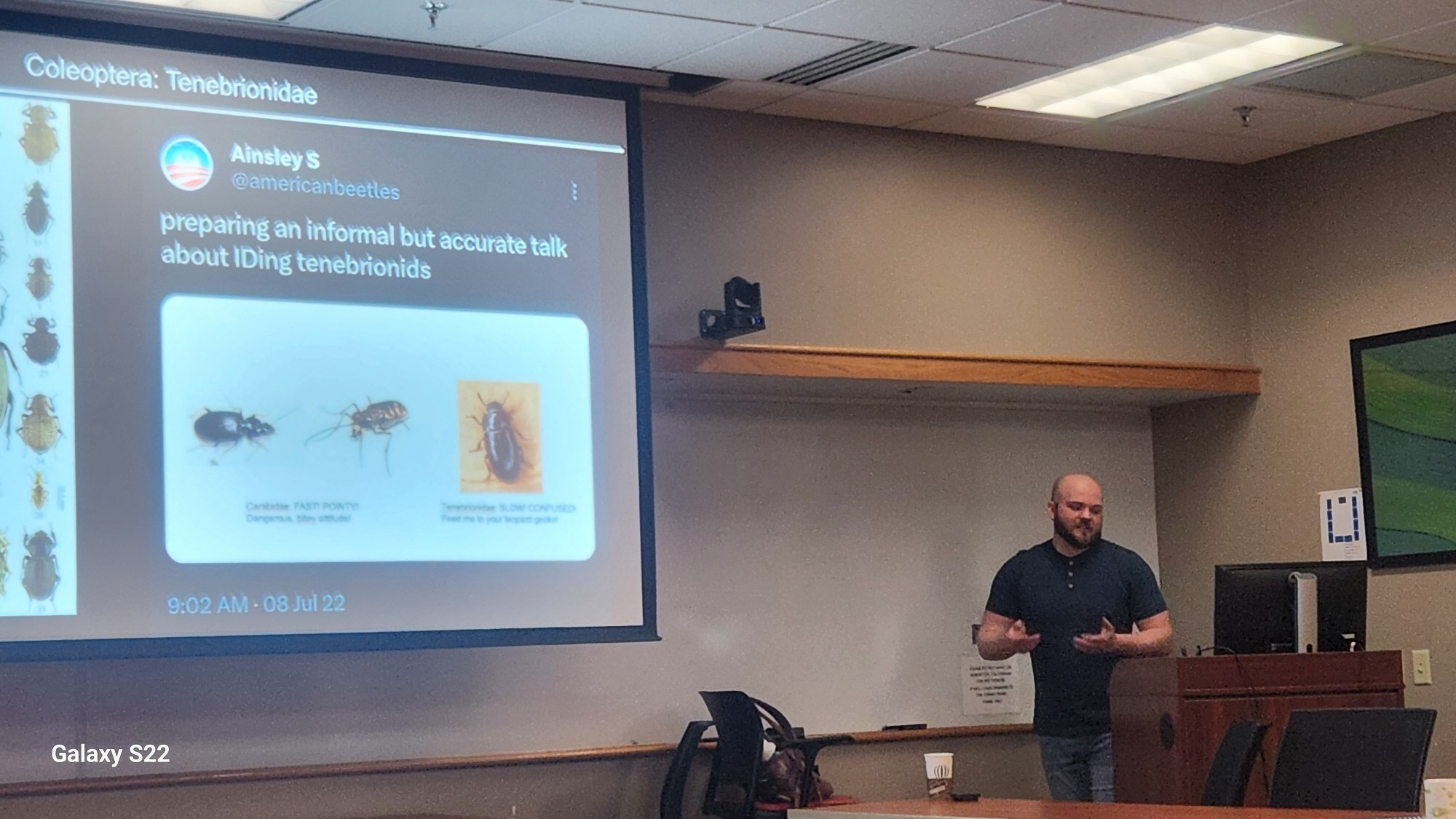 A man giving a scientific talk in front of a comouter, the slide he is talking about has a tweet from Ainsley S. about ground beetles and darkling beetles