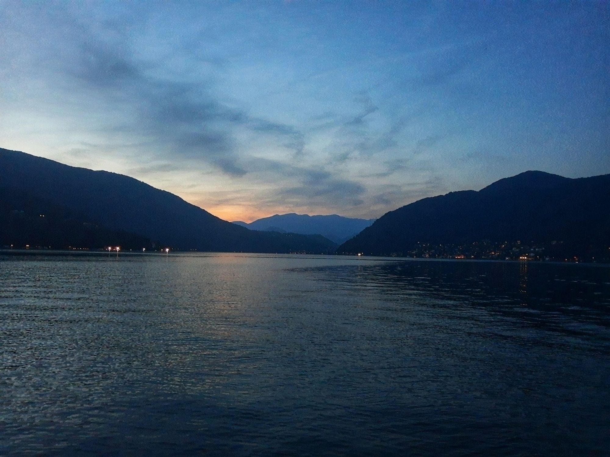 Auto-generated description: A tranquil lake is surrounded by mountains at dusk, with a soft glow visible on the horizon.