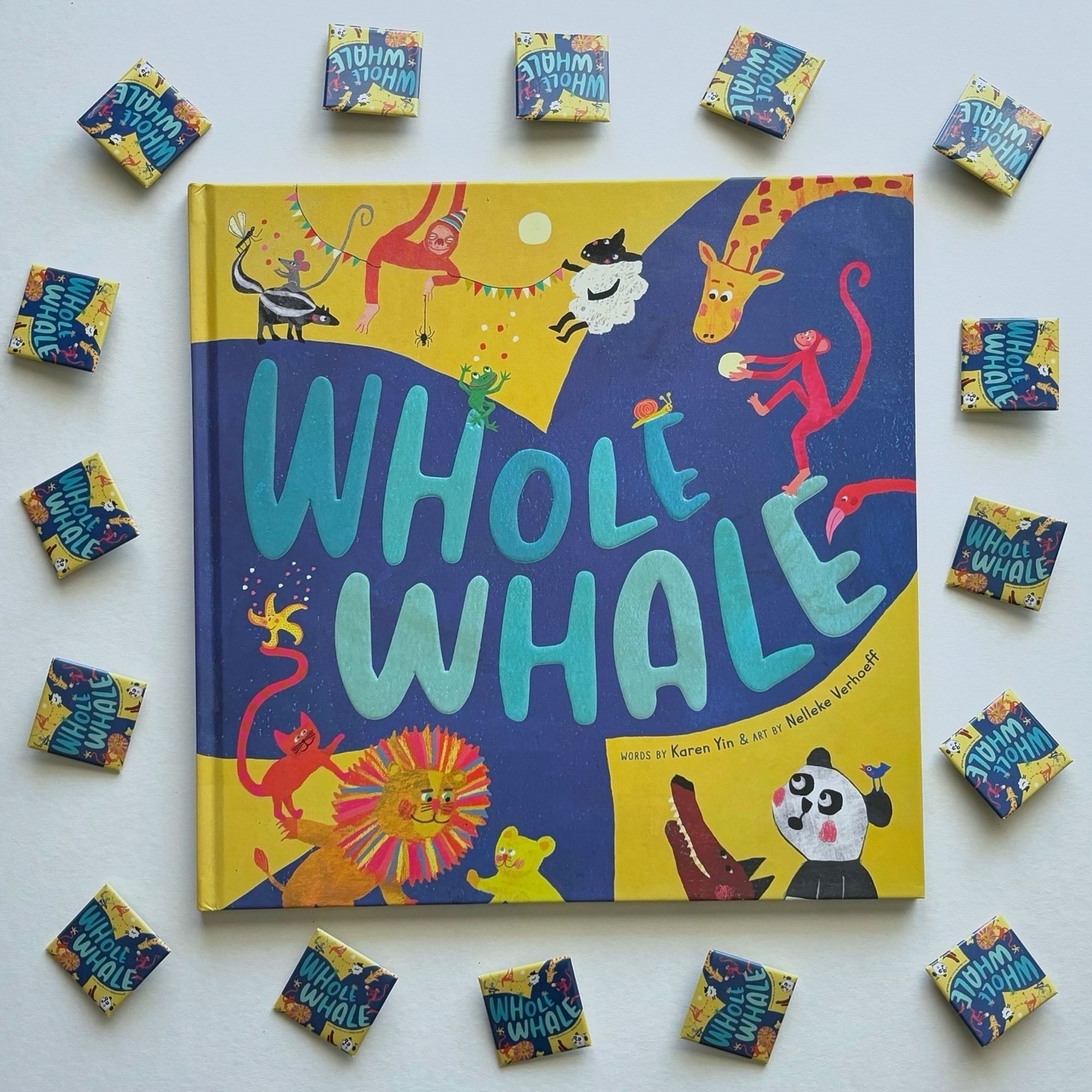 Square photo of a huge square book. Whole Whale has a bright yellow cover with a huge whale tail. The book is surrounded by cute square pins of the cover.