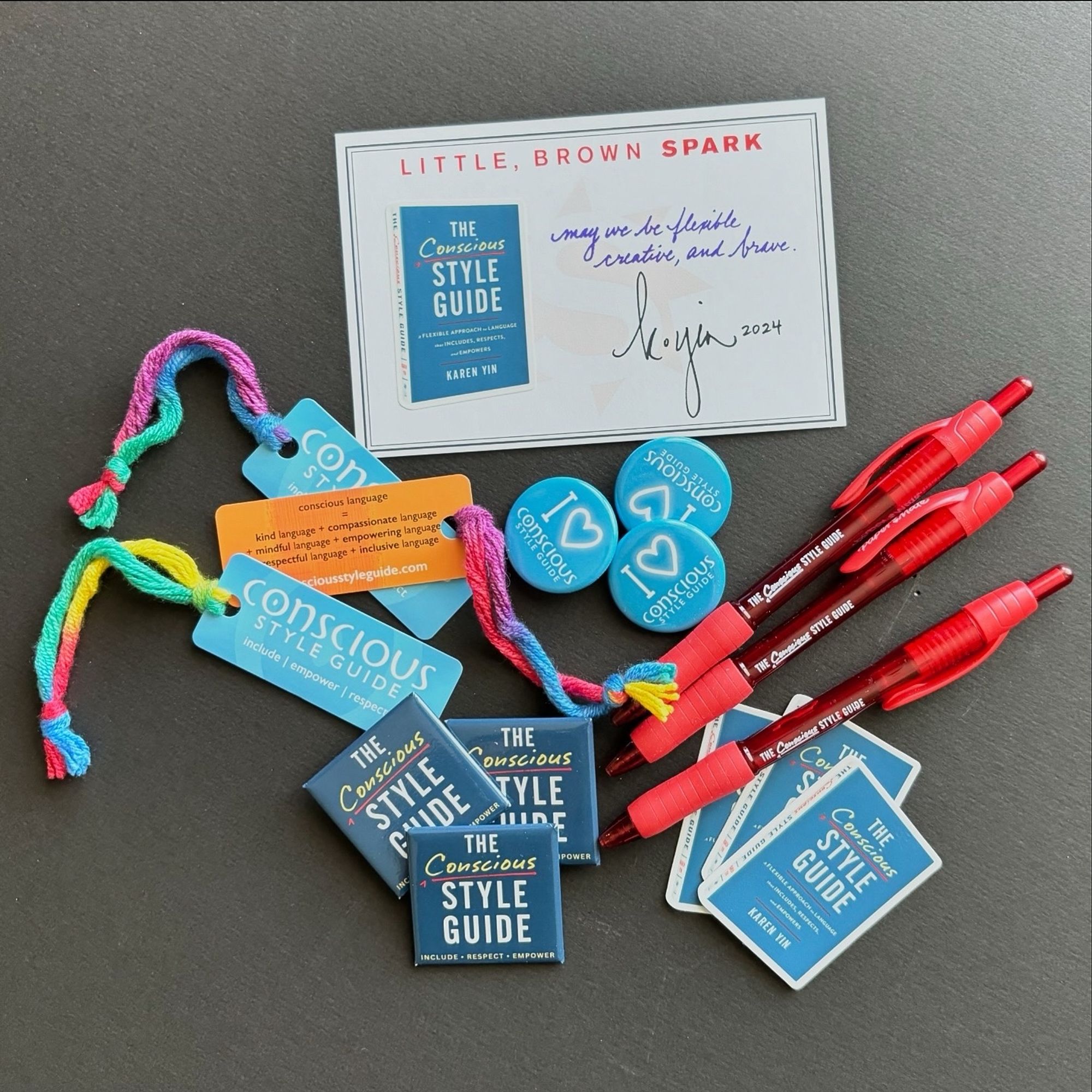 Overhead shot of swag for Conscious Style Guide the website and The Conscious Style Guide the book, including bookmarks, pins, pens, stickers, and bookplates.