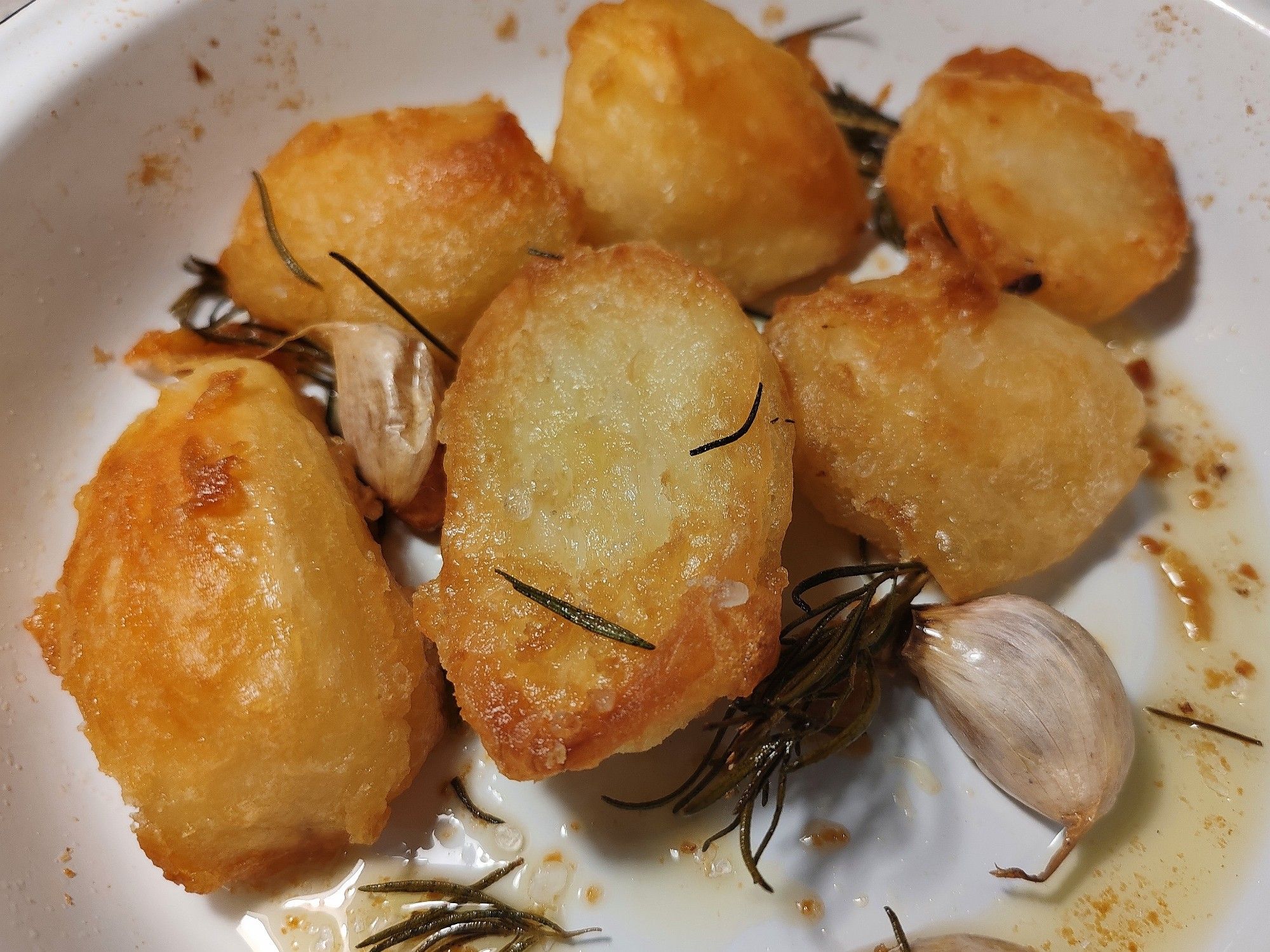 Seven golden and crispy roast potatoes with rosemary and garlic in a white enamel dish