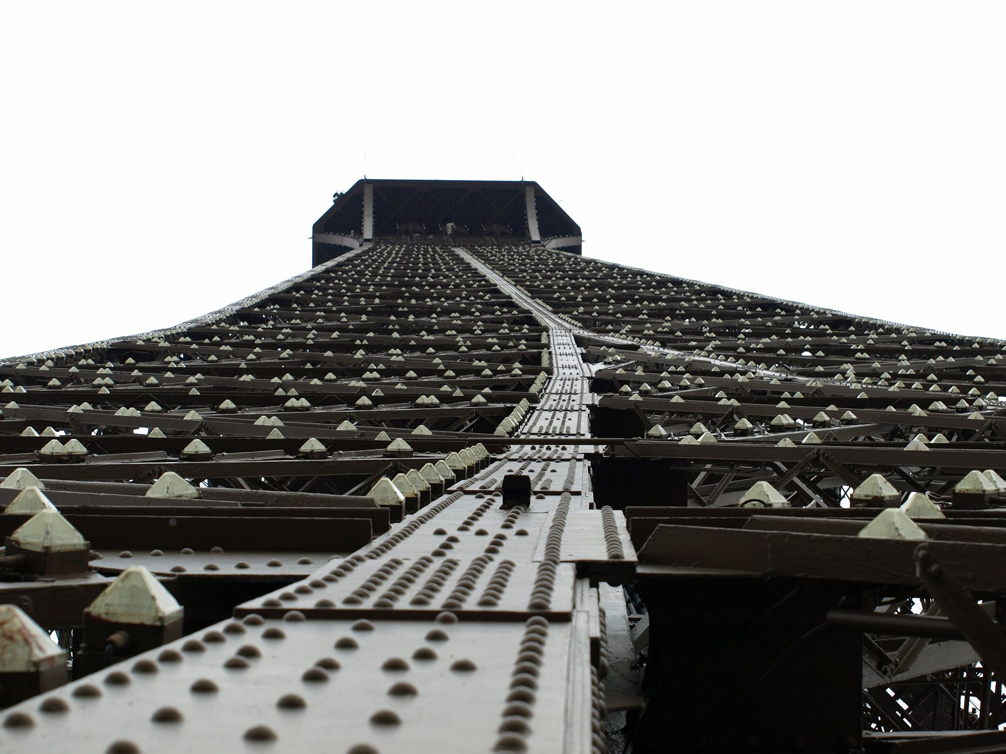 Blick nach oben entlang eines Beines eines Turmes aus Stahl. Man sieht unzählige Nieten und pyramidenförmige Erhebungen, die in hellem Grau gestrichen sind.