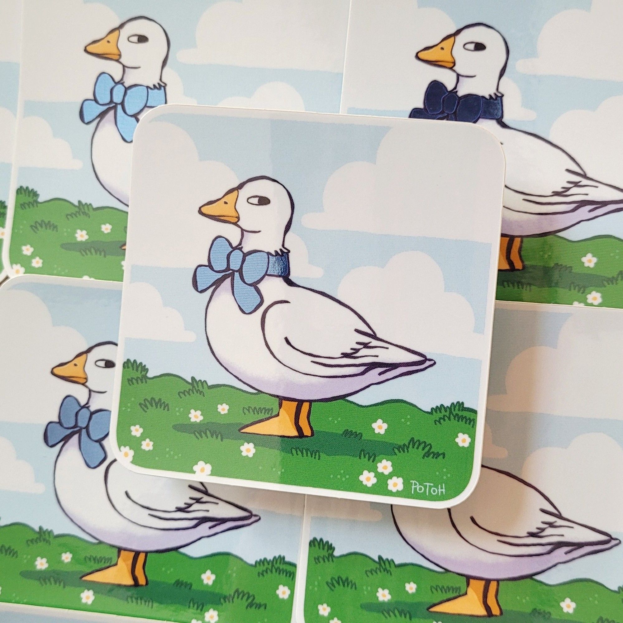 Photo of a slightly tilted rectangular sticker. The motive is a goose standing on green grass, wearing a blue bow tie and giving the onlooker a side-eye.