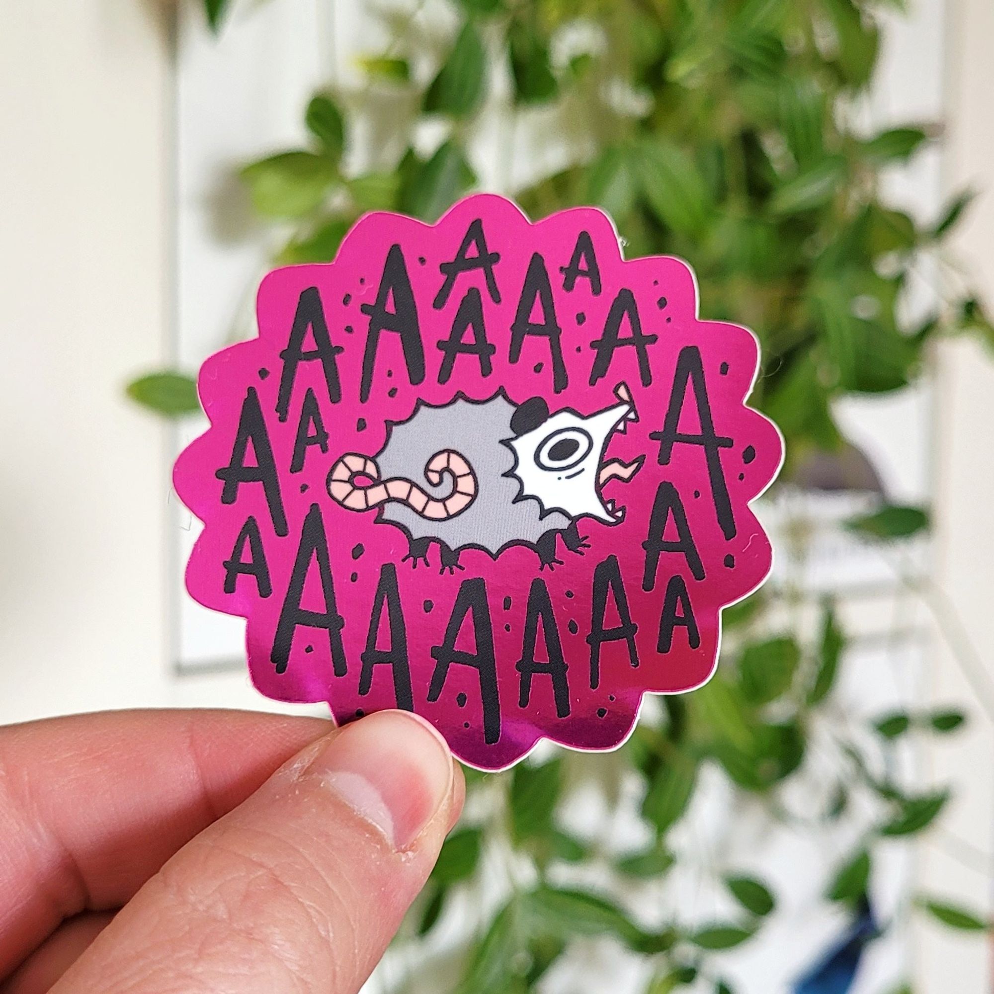 Photo of a dark pink sticker that shows a screaming possum in the middle, surrounded by the letter "A" several times.