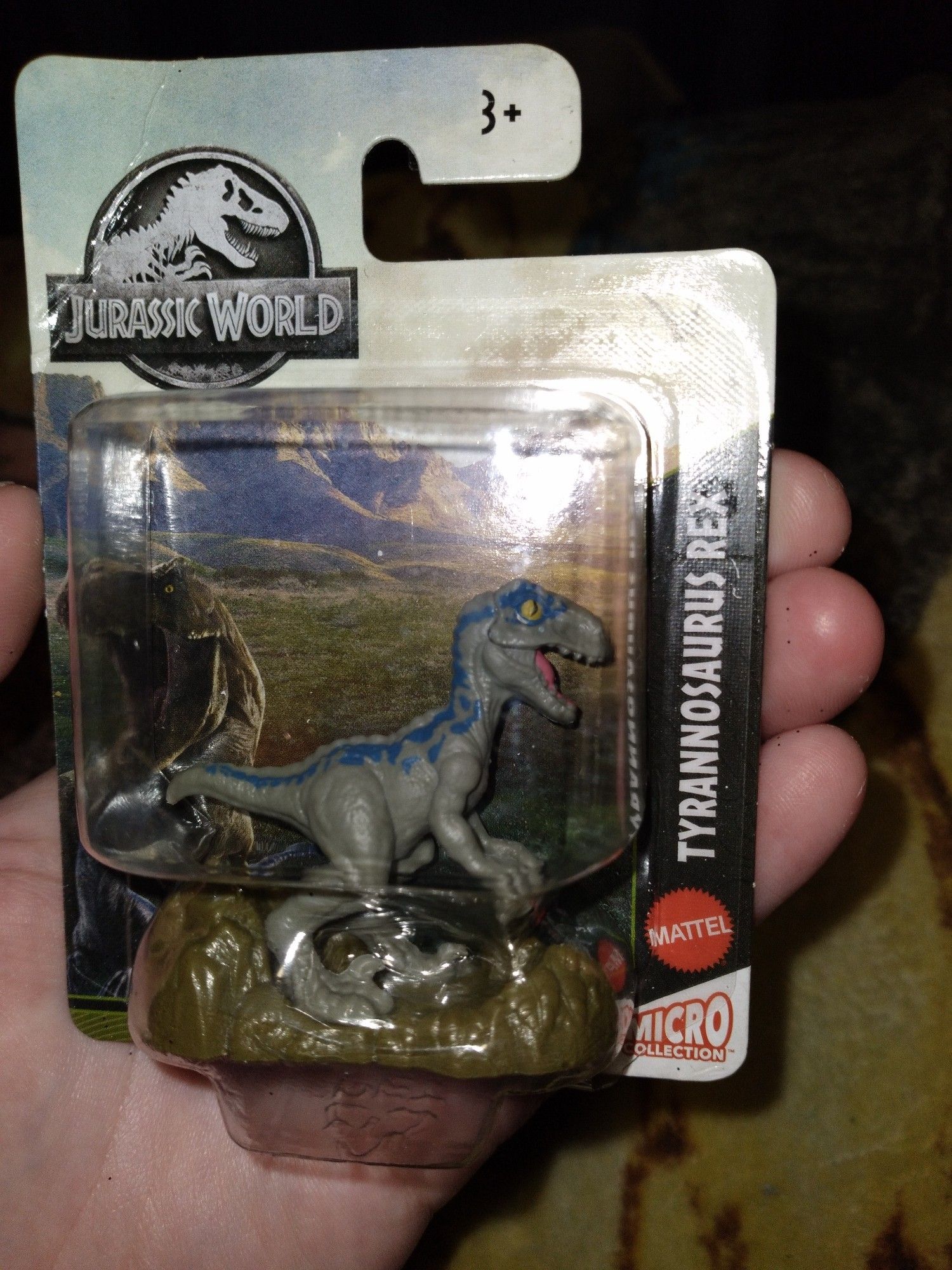 A mini figurine from the toy company mattel that labled the toy a t-rex but the acutal figure is of a raptor with blue markings on it, indicating it's one of the main dinos from the Jurassic World movies.