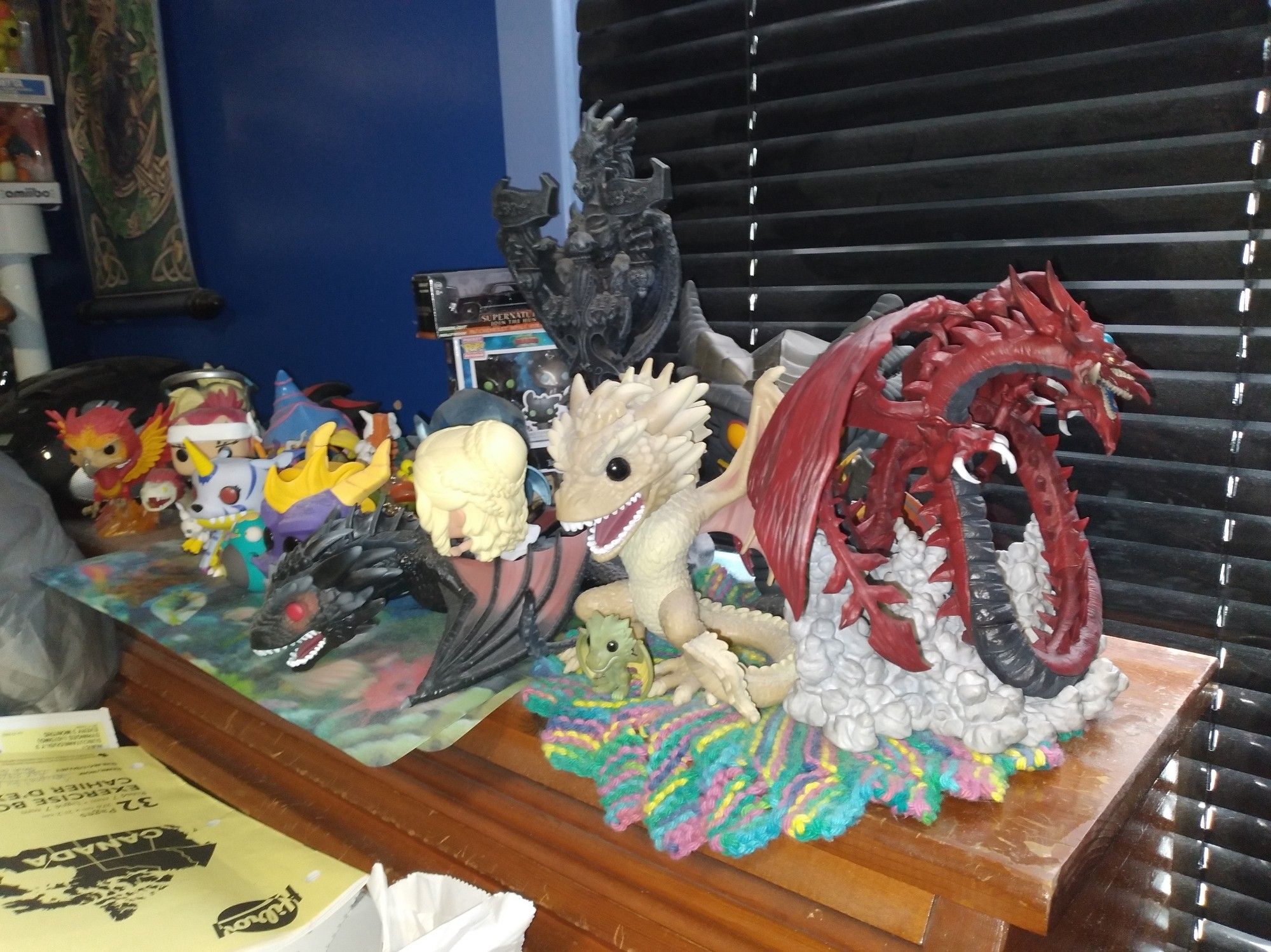 Photo showing a very messy desk with lots of funko pops n figurines, odds n ends statues n such but mostly showcasing the new edition of the Slifer the sky dragon figure that was added on the right end of the desk top area.