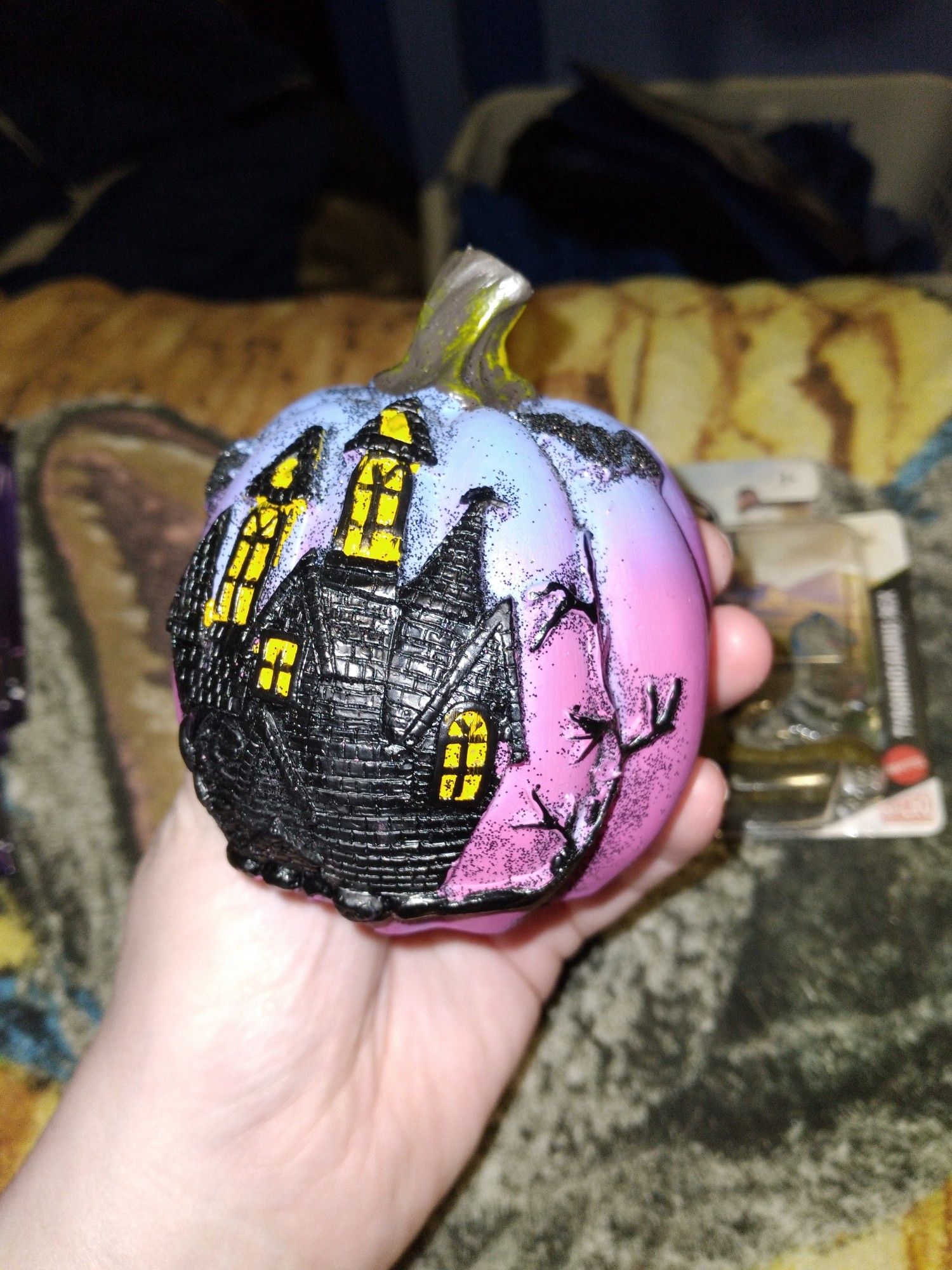 A mini purple n pink pumkin with a black painted spooky house with a tree n some bats flying around it, the black paint has a lot of sparkly black stuff on it!