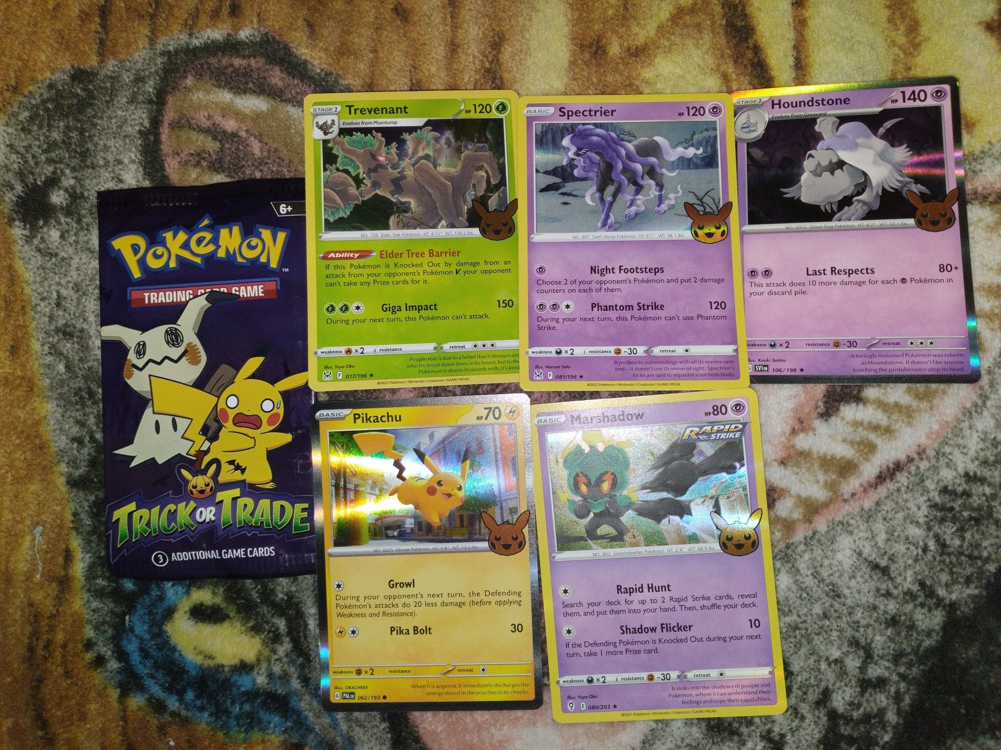 Pokemon holo cards pulled from packs in order: a green card holo if a ghost tree called Trevenant, a purple holo card with a shadow horse called Spectrier, a purple holo card with a undead dog called Houndstone, a yellow holo card with a cute little yellow mouse named Pikachu and another purple holo card with a very punchy ghost named Marshadow.