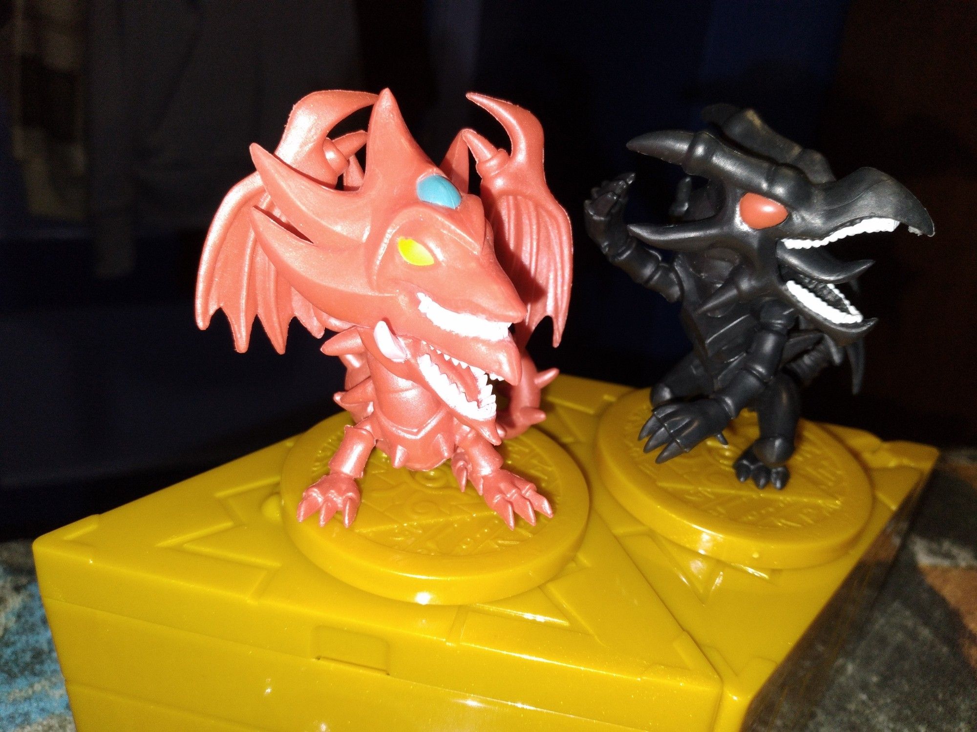 A left side view of a close up of the mini chibi yugioh figurine charactes..left is Slifer the sky dragon and right is Red-Eyes black dragon.