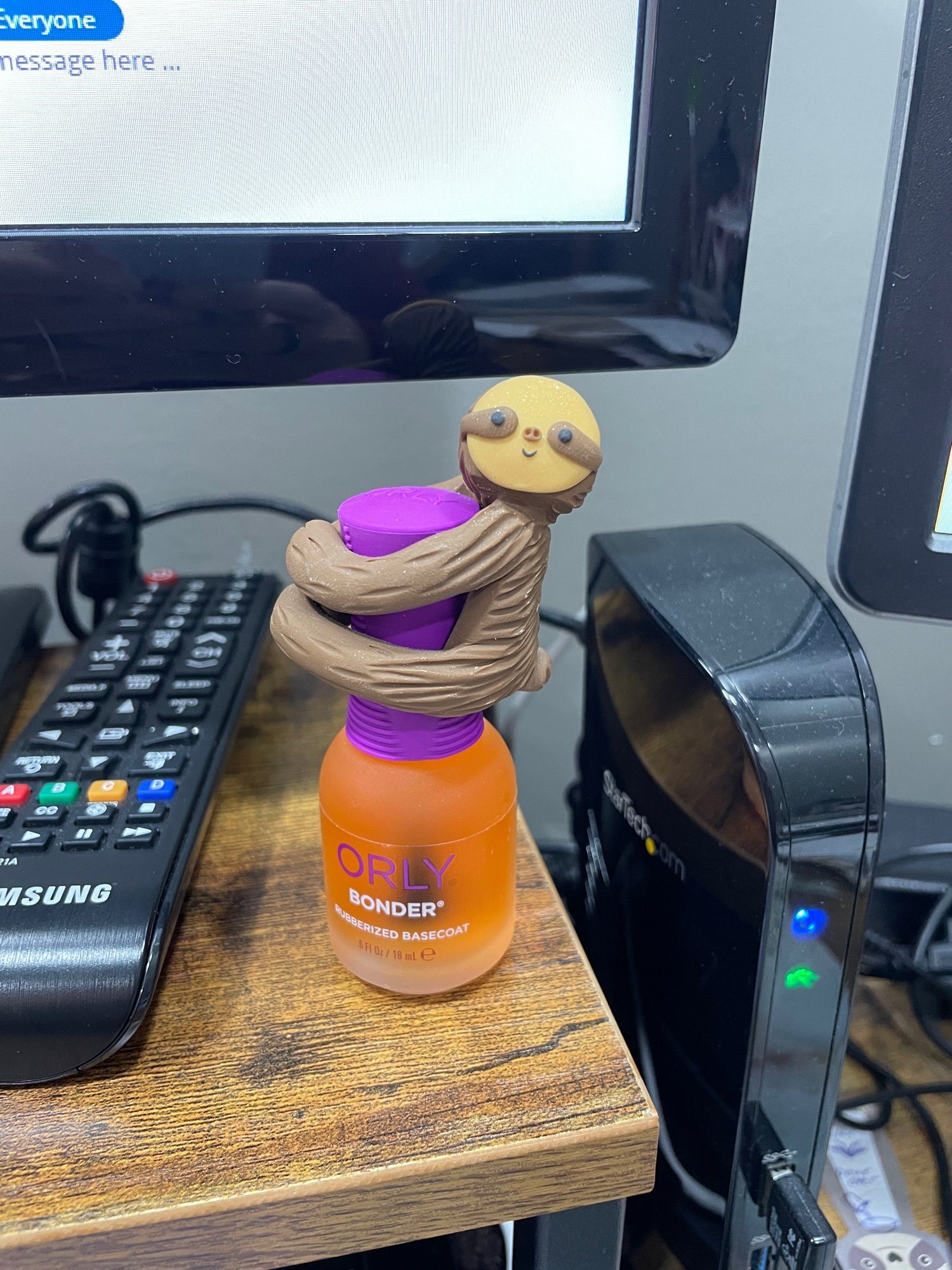 A small clay sloth hugs the handle of a nail polish bottle on a desk.