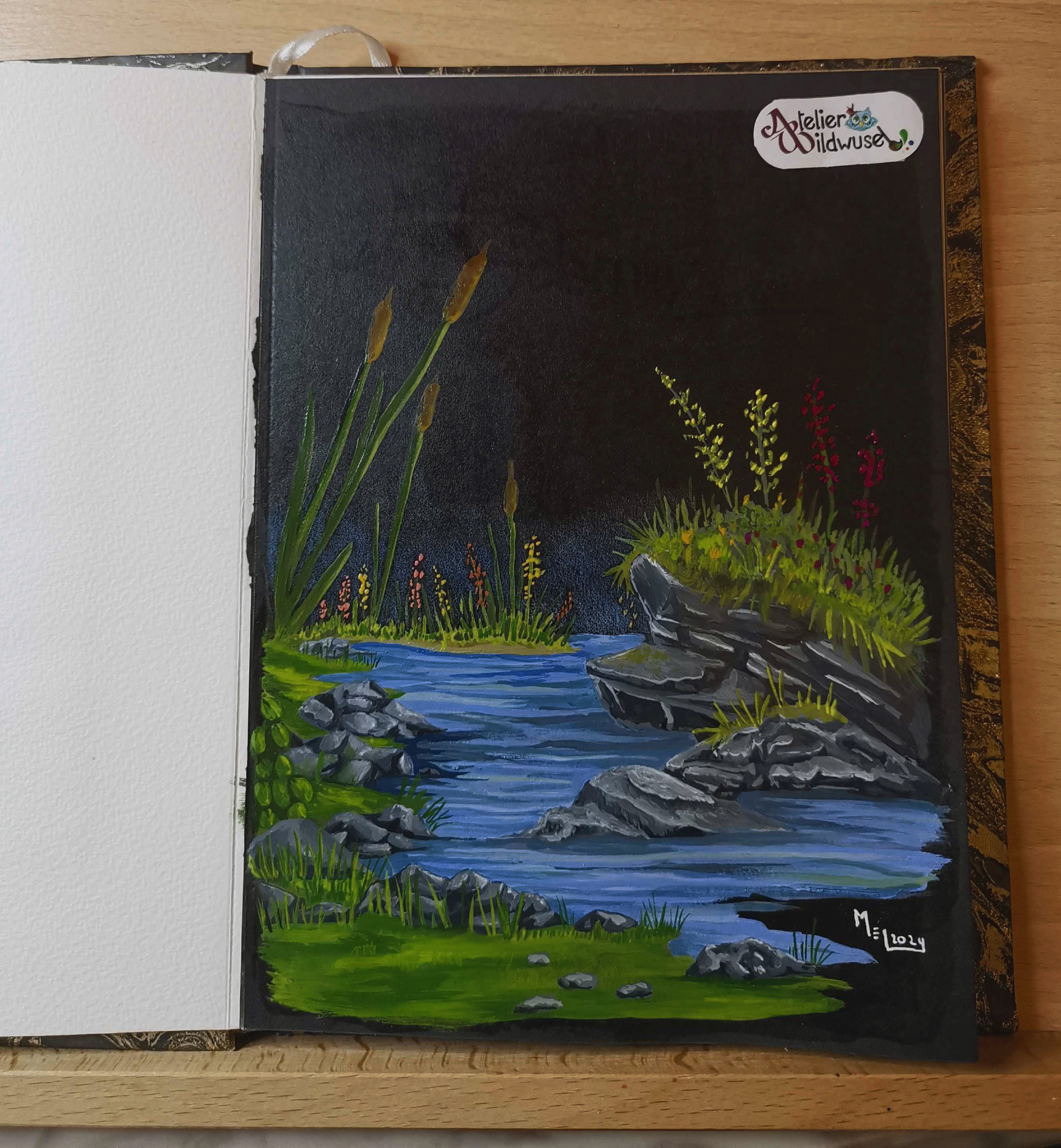 Schwarze Skizzenbuchseite mit einer Gouache Malerei: rechts sind einige Steinformationen zu erkennen, auf dene Gras und  blaue, wie gelbe Blumen  ( etwas wie Wiesensalbei oder Lavendel nur in Violett und gelb). Darunter  und um die Steine herum fliest ein ruhiges Gewässer ( vielleicht ein Ausschnitt eines Baches oder Teichs). Auf der linken Seite ist das Ufer zu sehen mit einzelnen Steinen die ins Wasser ragen sowie Grünpflanzen und Gras.