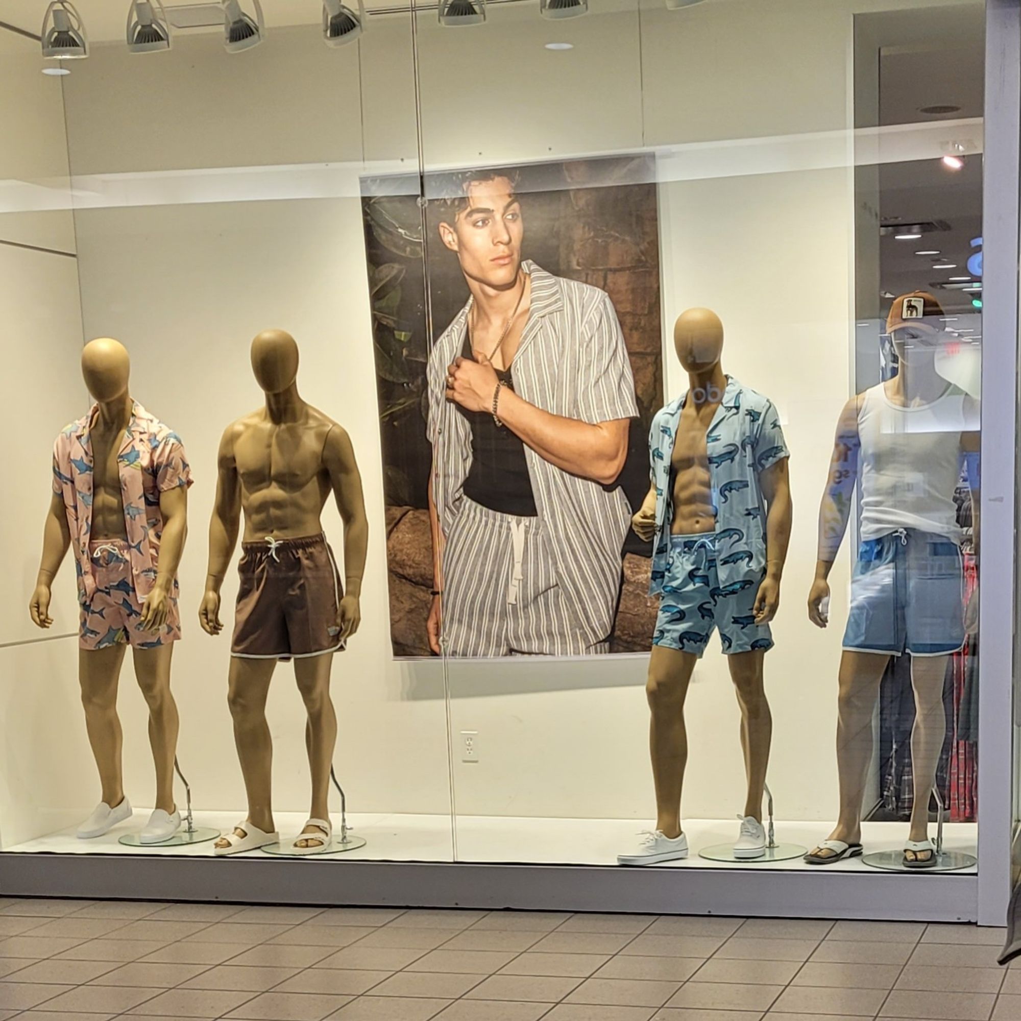 Four male mannequins in shorts and unbuttoned short sleeve shirts. They all have six packs and an unmistakable aurora of gayness