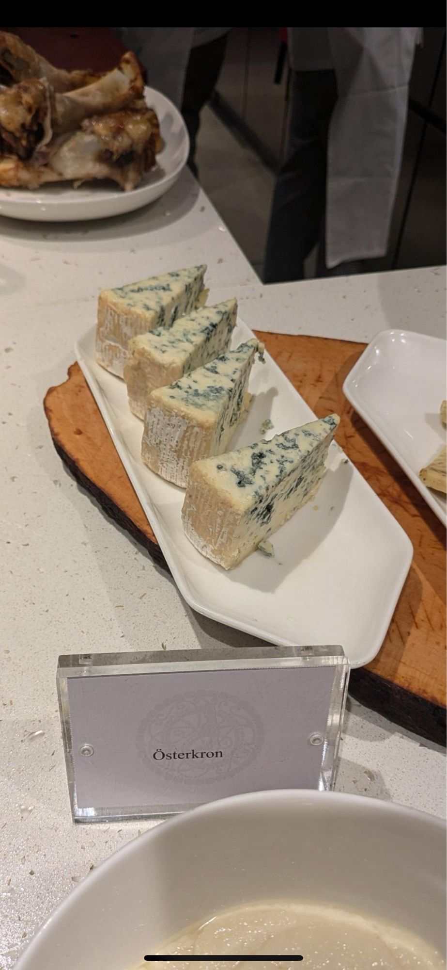 Wedges of blue cheese on a white plate, behind a card identifying it as Österkron.