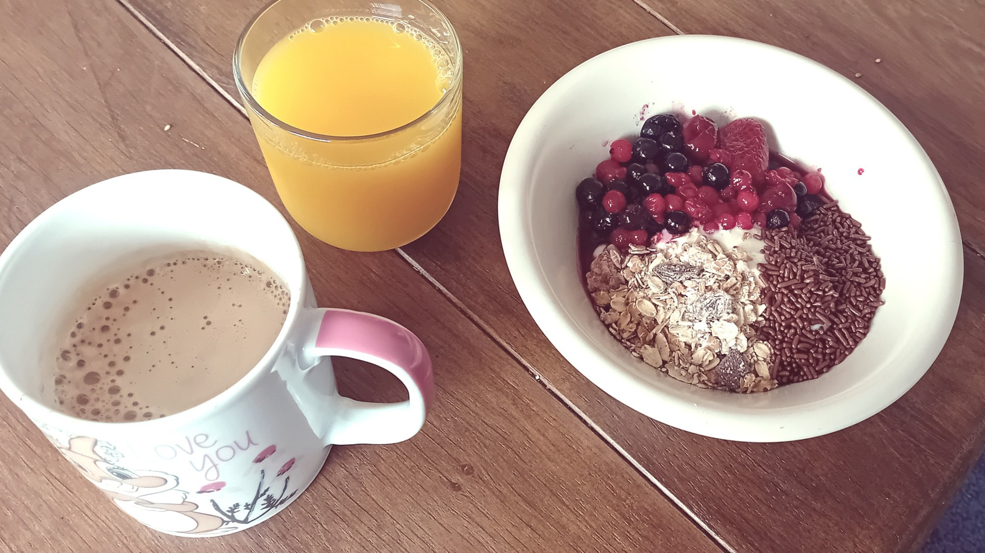 Ontbijtje bestaande uit eem grote mok koffie, een klein glas sinaasappelsap en een schaaltje met kwark, bosvruchten, hagelslah en muesli.