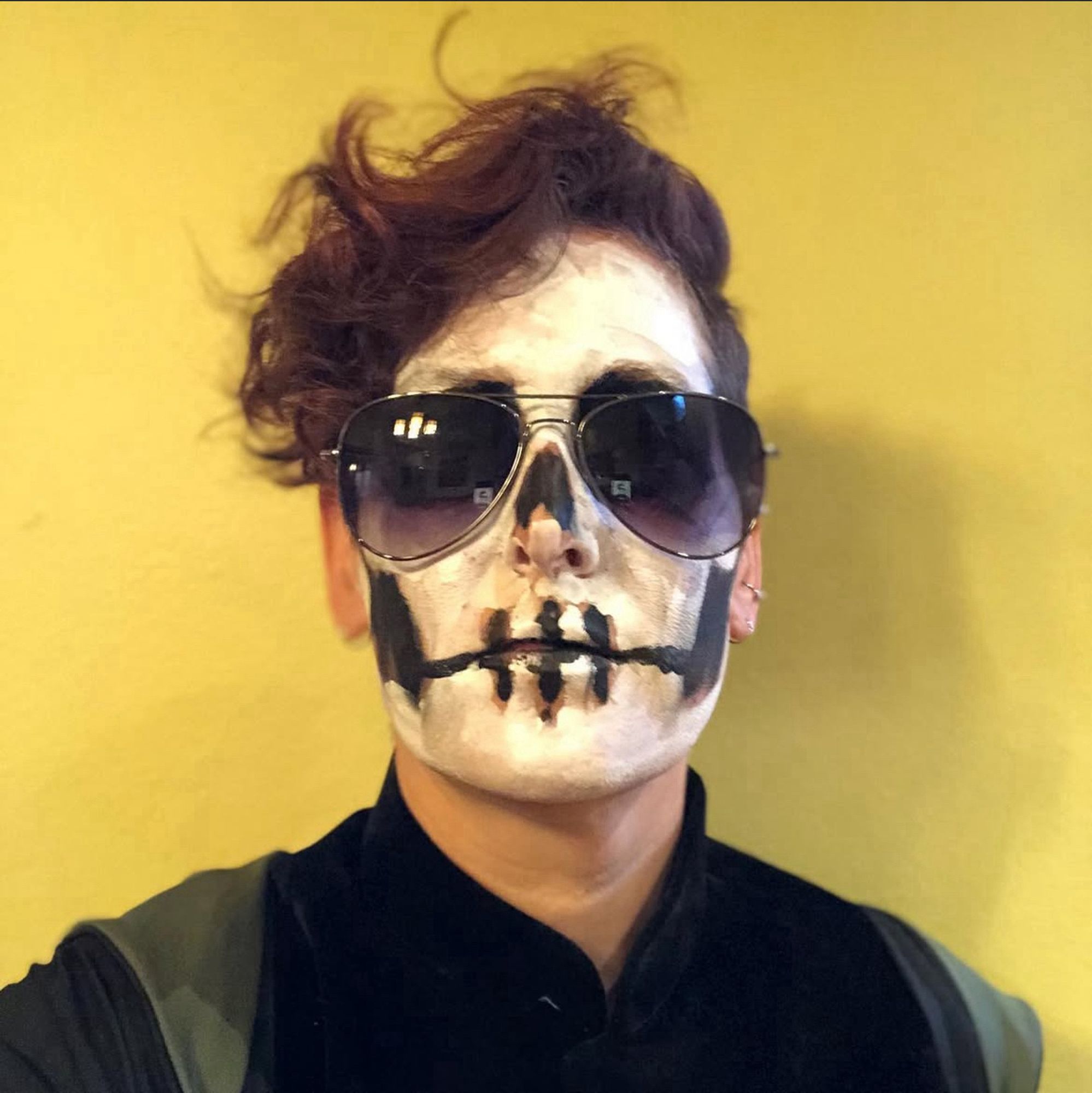 Me dressed as Gideon Nav from Tamsyn Muir’s fantastic book “Gideon the Ninth”. My hair is shaved on the sides and wavy on the top, and I have sprayed it read. I have badly painted skull makeup on my face and am wearing oversized aviator sunglasses, a black shirt and a robe.