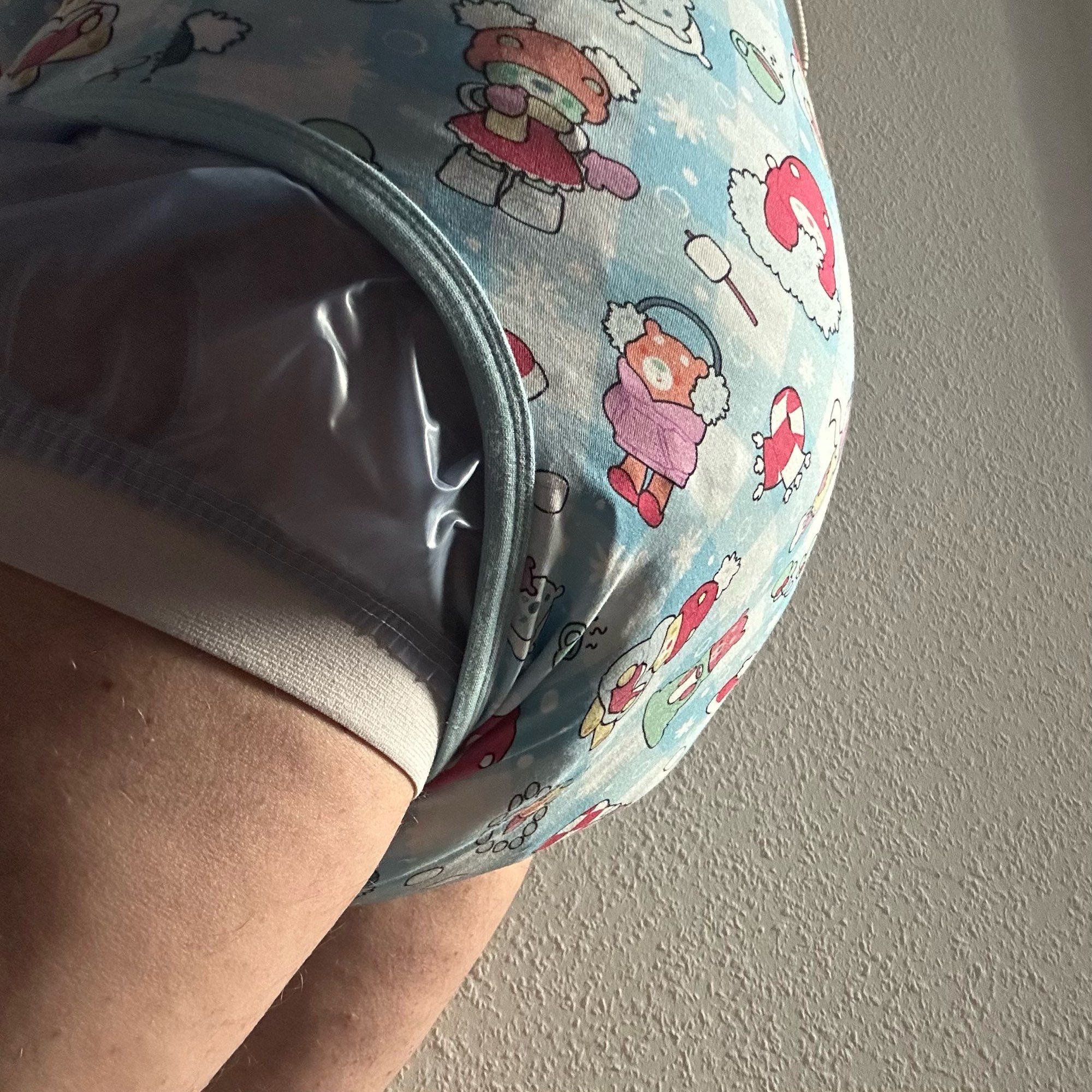 You see the hiney of a person and their upper thighs in side view that is wearing a soggy sagging diaper underneath a onesie and an overpants.