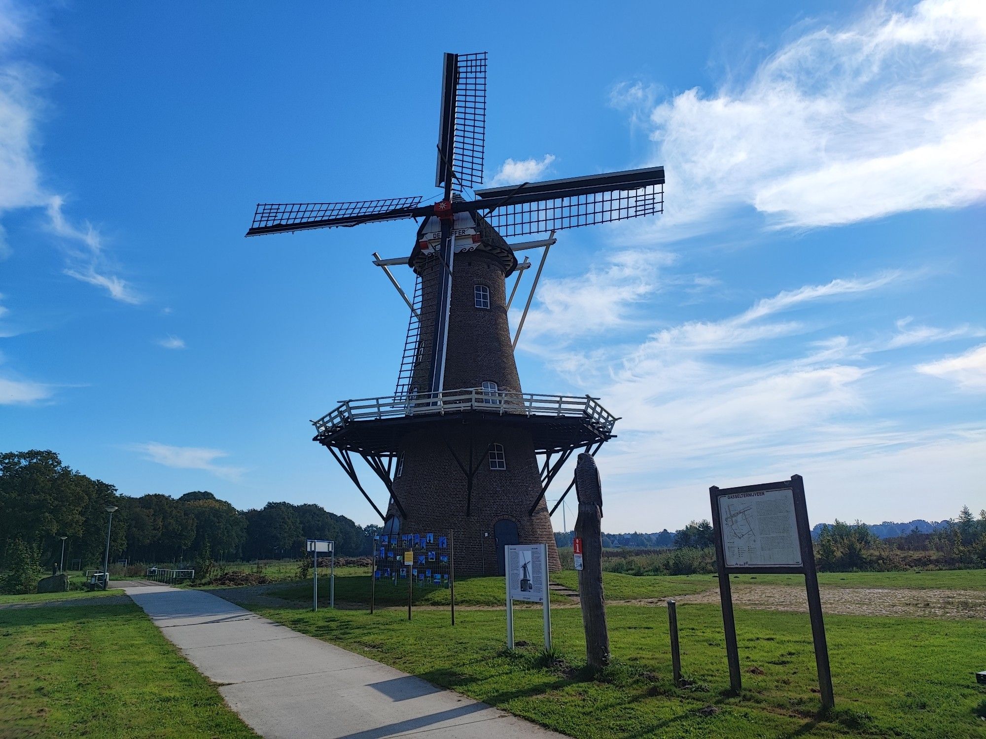 Ein Radweg zwischen Gieren und Stadskanaal. Links vom Radweg ist um Vordergrund eine Wiese zu sehen. Im Hintergrund stehen Bäume. An der Rechterseite steht eine alte traditionelle niederländische Windmühle auf eine Wiese.